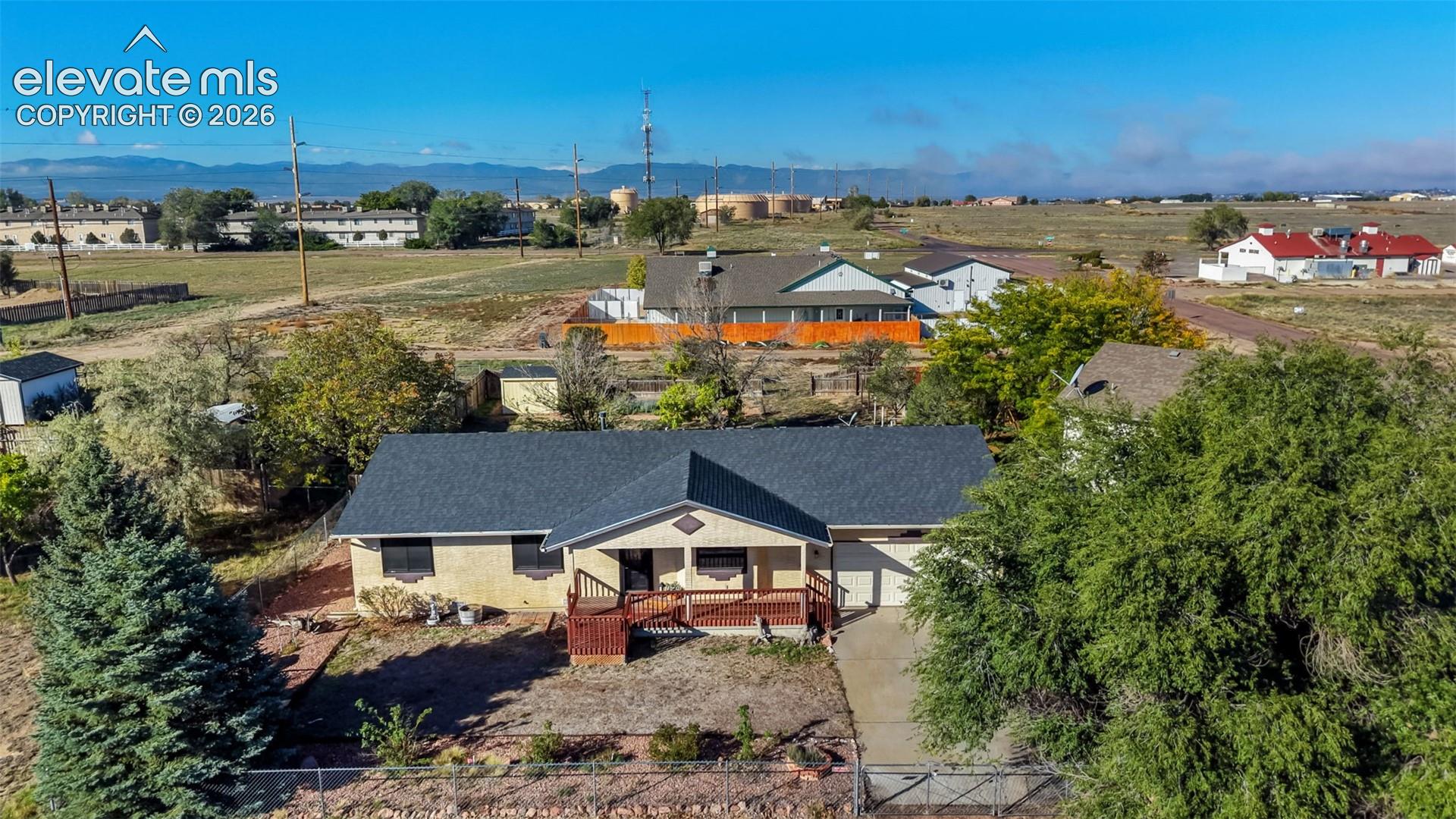 Single-story residence featuring a dark shingled roof, stucco exterior, covered front porch, attached garage, and mature trees on the lot