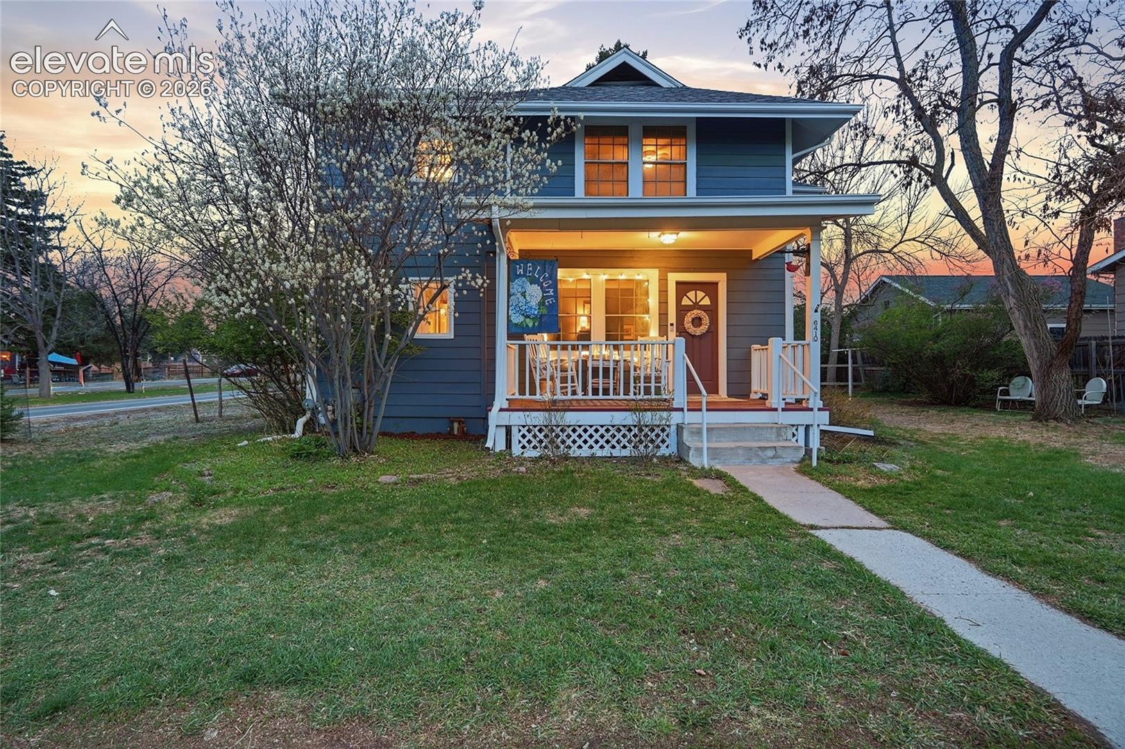 Two-story exterior with horizontal siding, covered front porch, wooden railing, lattice skirting, and a concrete walkway