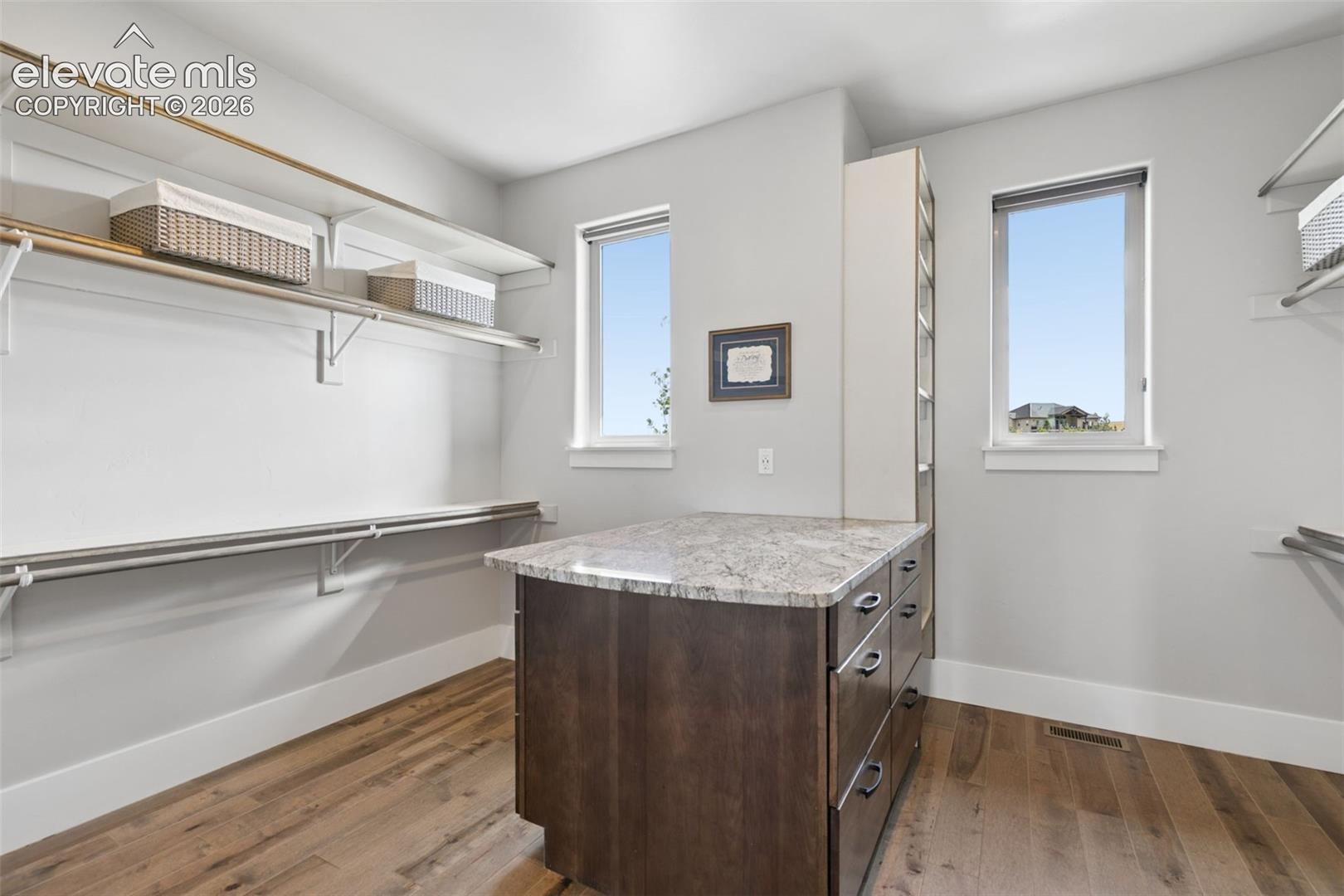Custom closet island with stone-finish countertop, wood-finish flooring, and two windows