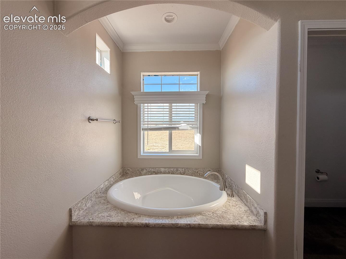 Built-in soaking tub with a patterned stone-surface deck, arched recessed ceiling, and curved faucet fixture