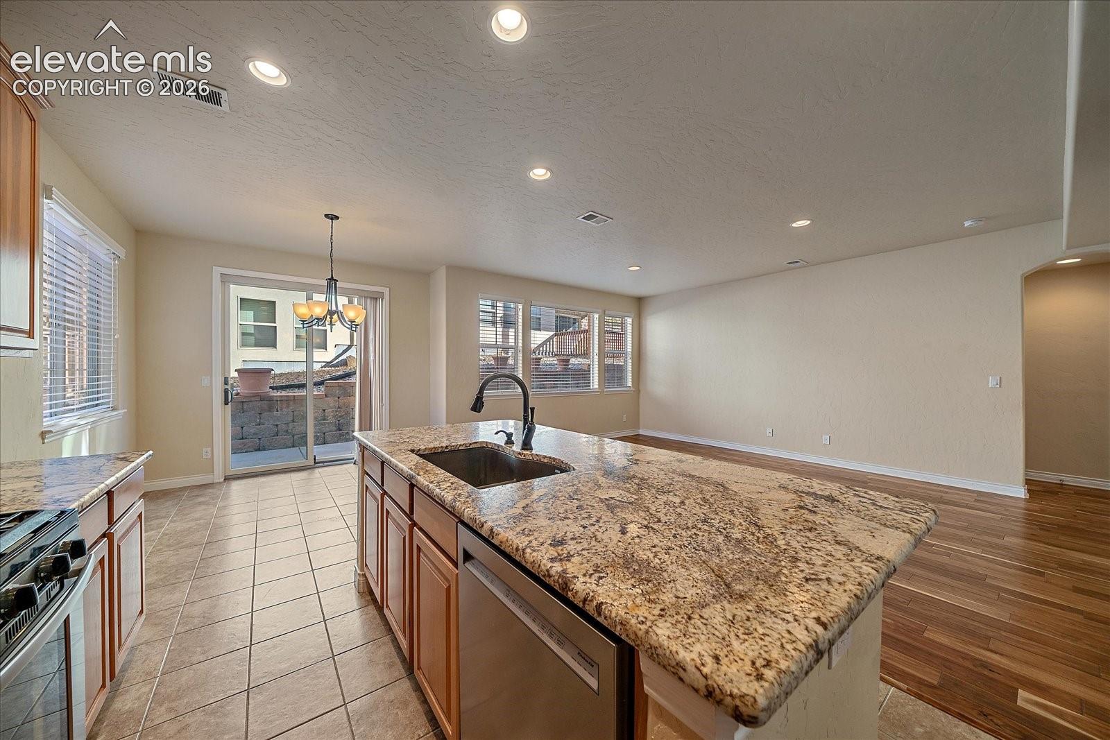 Kitchen featuring a central island with a stone countertop, under-mount sink, stainless steel dishwasher, tile flooring, and recessed lighting