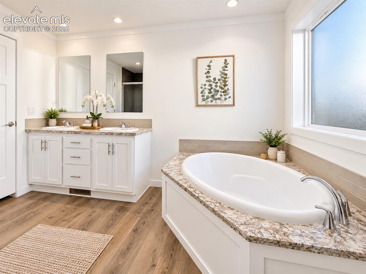 Primary Bathroom – Spacious primary bath features a double-sink vanity, soaking tub with surrounding ledge, generous cabinetry, and natural light from a large window.