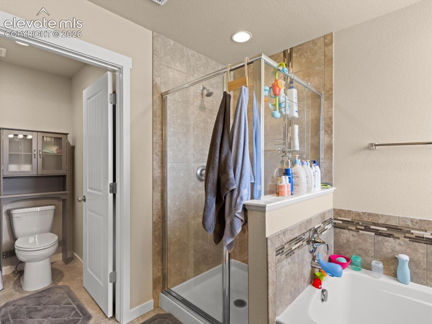 Spacious bathroom featuring a glass-enclosed shower, built-in bathtub, and an alcove for a toilet