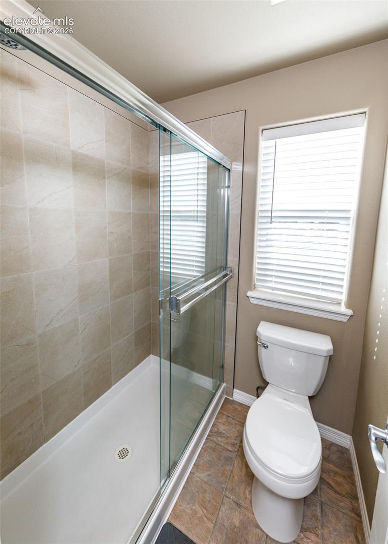 Walk-in shower with sliding glass enclosure and tiled surround, accompanied by a high-efficiency toilet and tile flooring