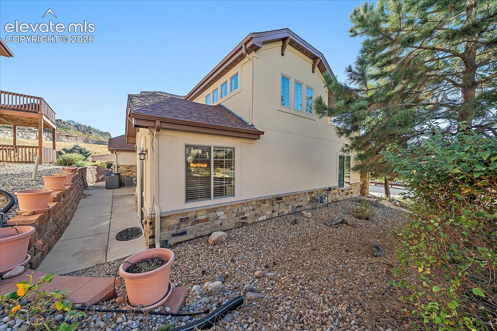 Stucco exterior featuring stone veneer accents, multi-gabled roofline, concrete walkway, and rock landscaping