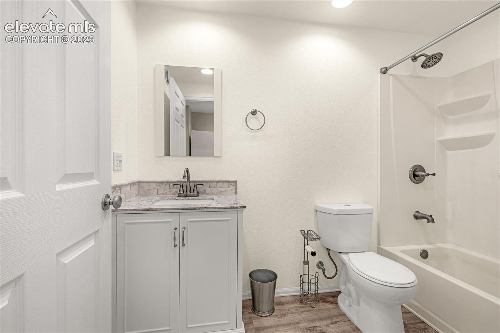 Bathroom featuring a white shaker-style vanity with a stone-finish countertop, integrated sink, wood-finish flooring, and a tub-shower combination with a molded surround