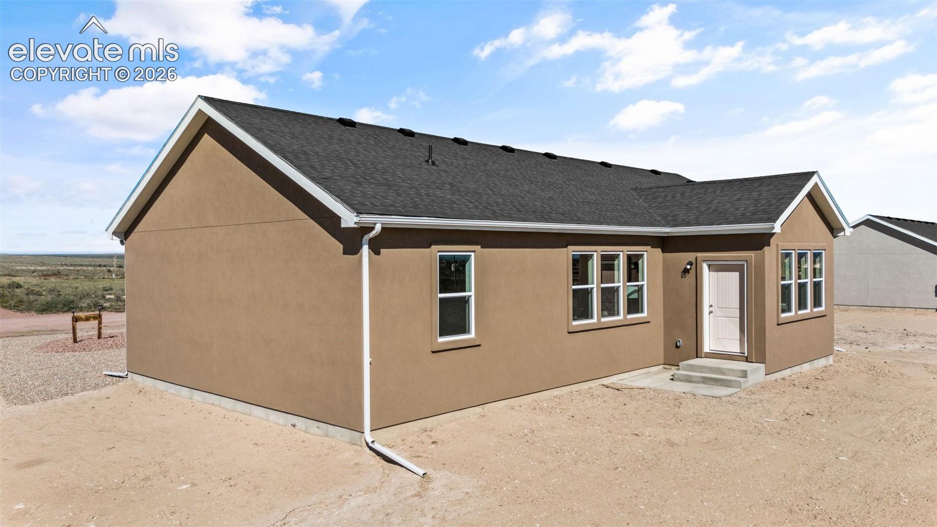 Stucco exterior with a dark shingle roof, white window trim, and white gutters