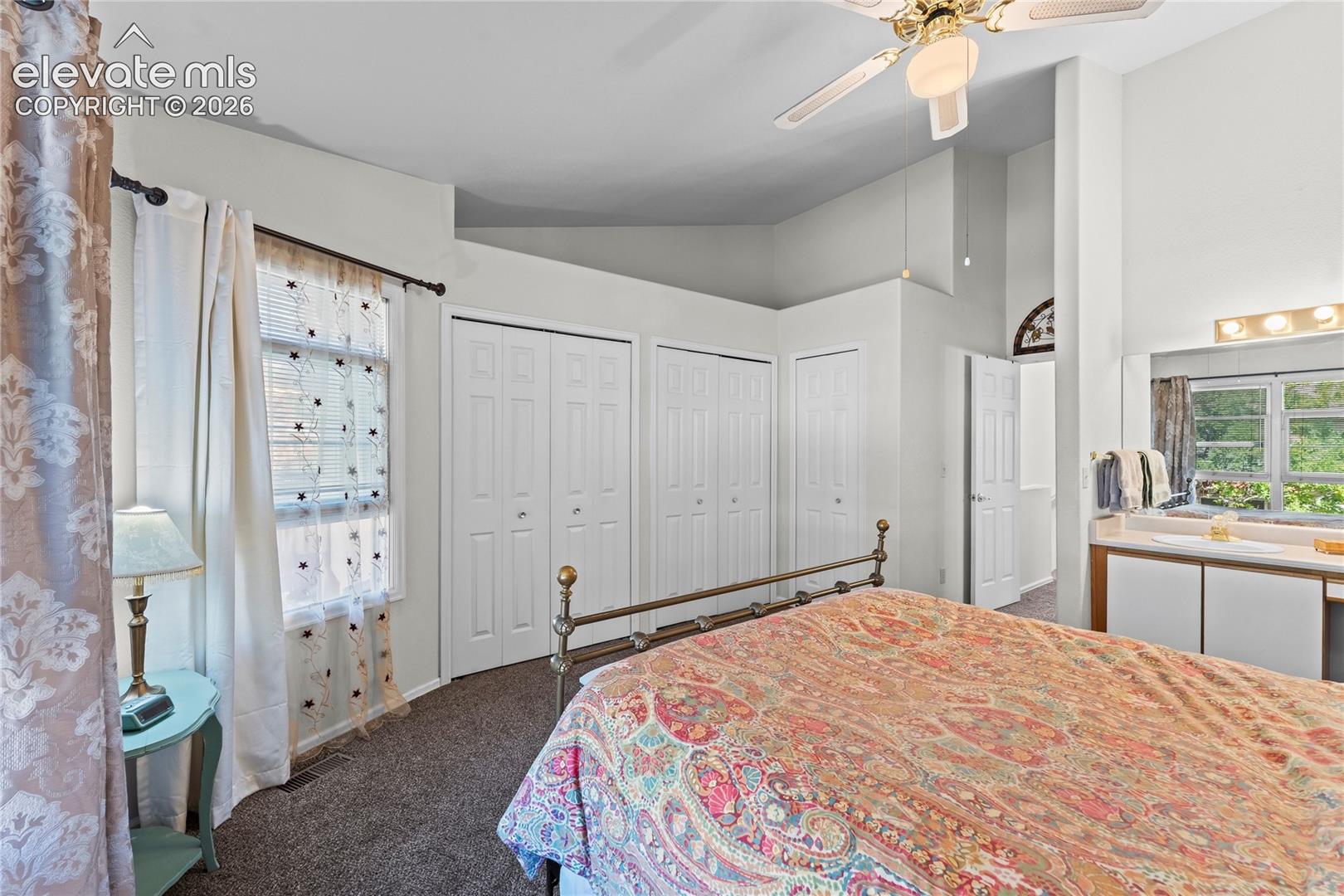 Carpeted bedroom featuring a ceiling fan with integrated lighting, multiple paneled closet doors, and an integrated vanity with overhead lighting