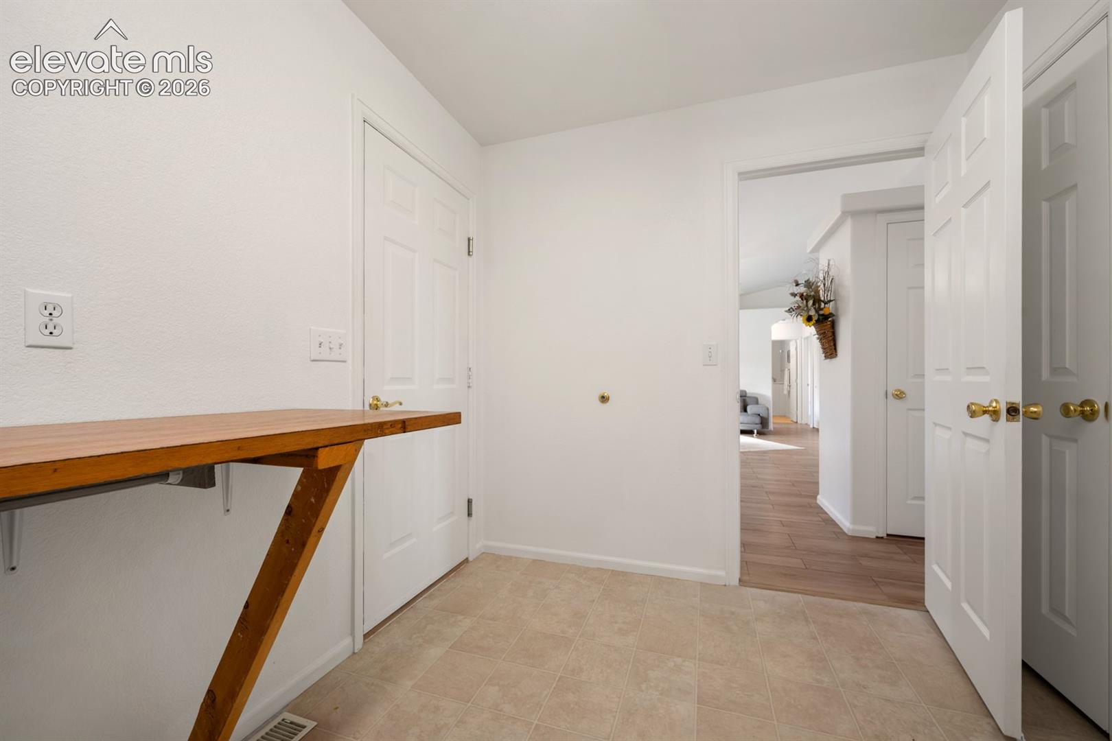 Entryway featuring light-toned tile flooring, a wall-mounted wooden surface, and white six-panel interior doors with metallic hardware