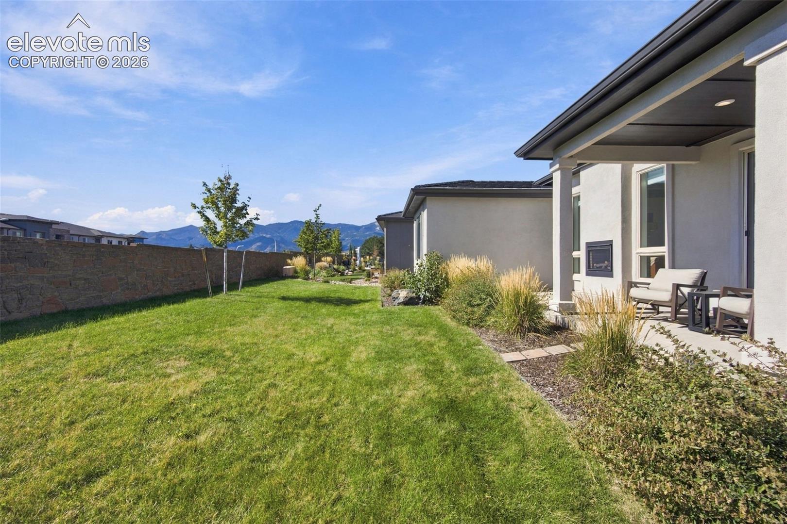 Backyard featuring a covered patio, a masonry privacy wall, manicured lawn, landscaping beds, and mountain scenery
