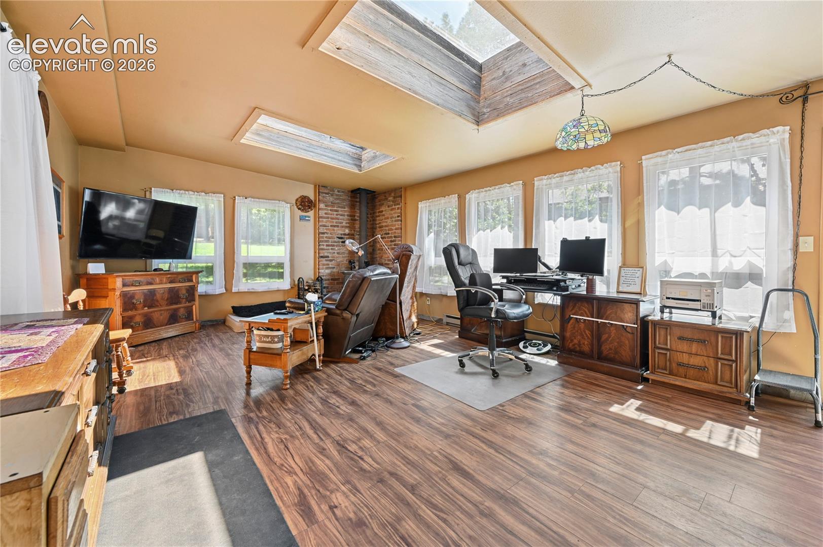 Wood-finish flooring, multiple skylights, and a brick accent wall complement the abundant natural light from numerous windows