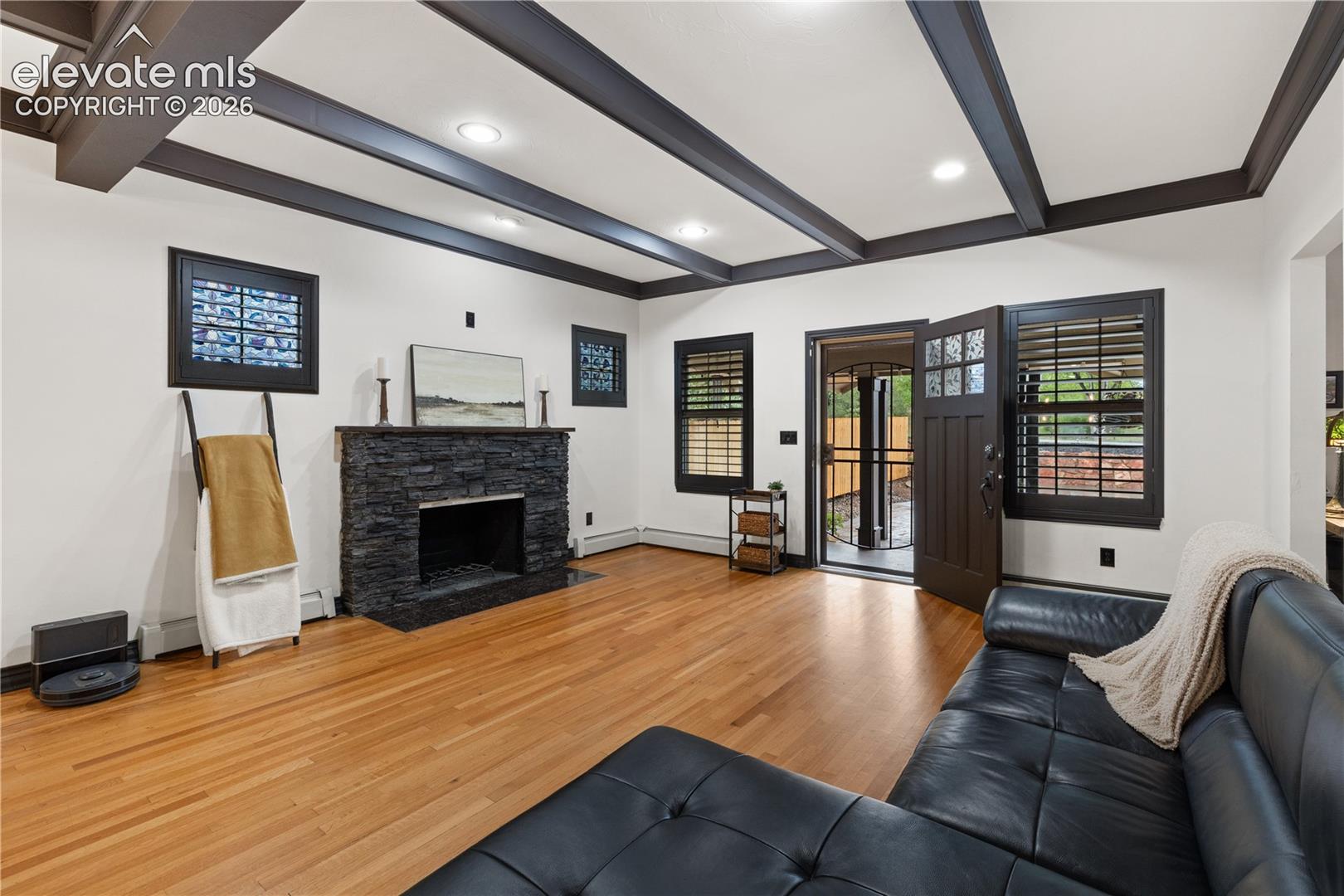 Living space featuring wood-finish flooring, a stone-clad fireplace, and beamed ceilings