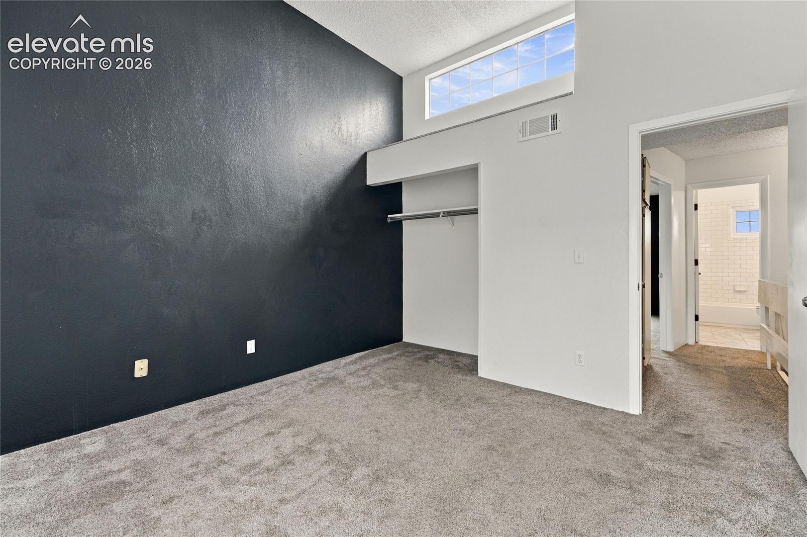 Vaulted ceilings featuring a transom window, wall-to-wall carpeting, and a built-in closet with integrated shelving