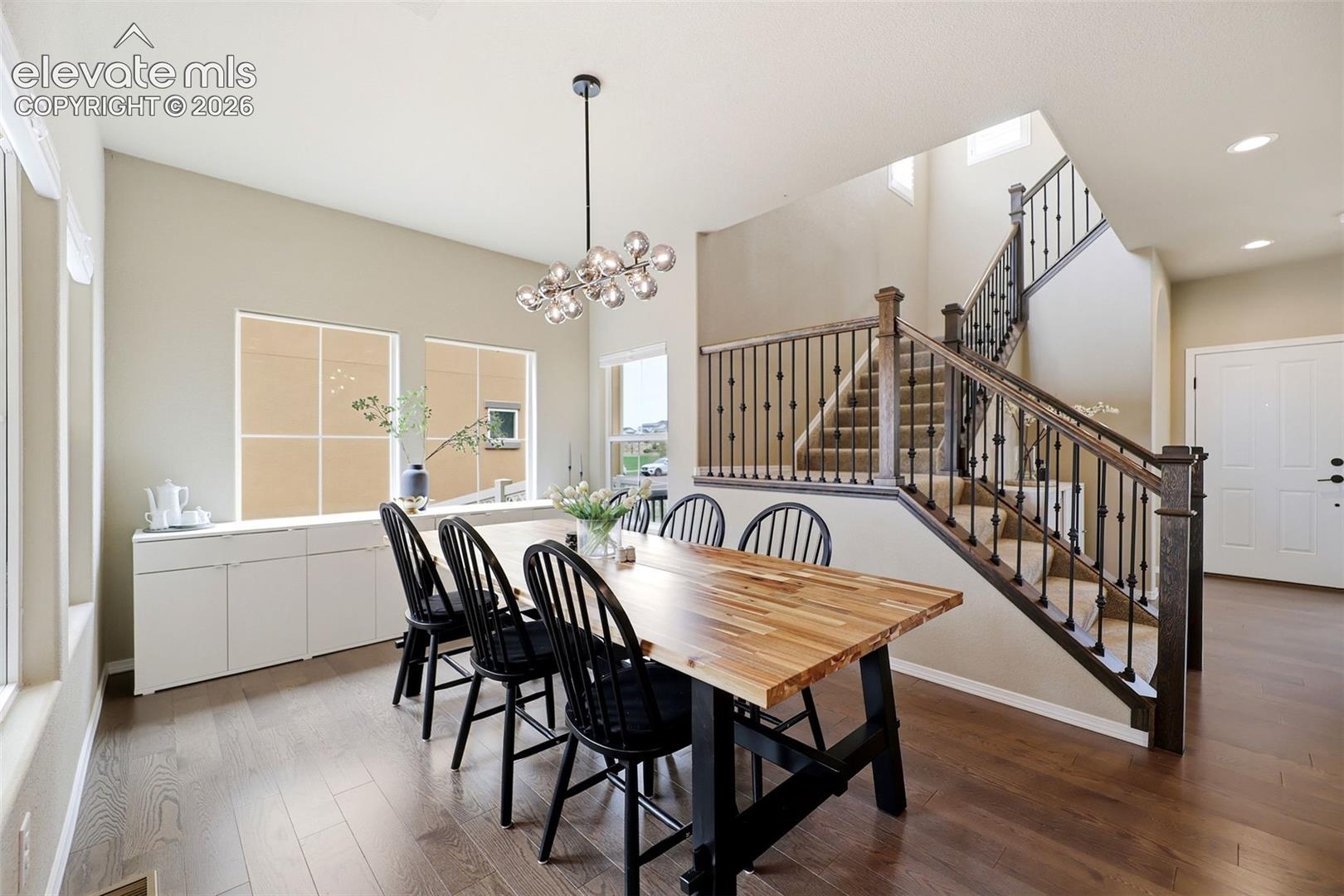 Wood flooring, staircase with dark wood banister and wrought iron balusters, vaulted ceiling, built-in white cabinetry, and modern linear chandelier