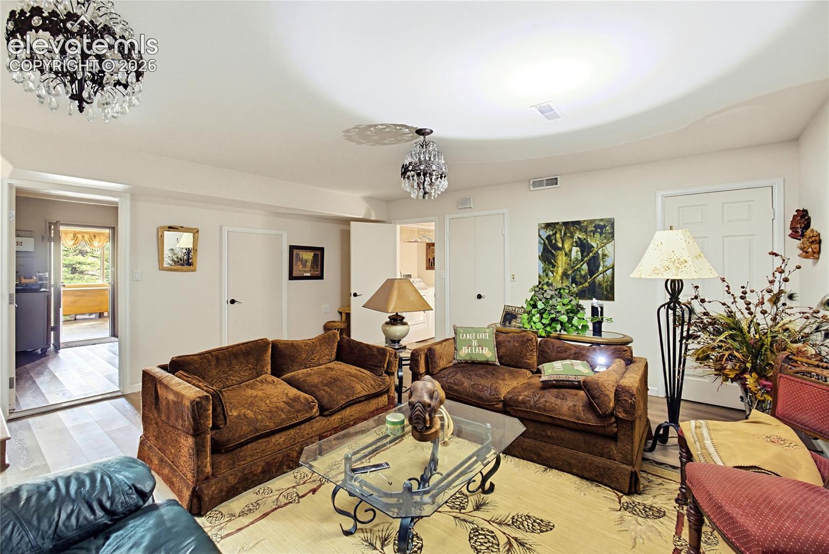 Living area featuring recessed tray ceiling, two crystal-style chandeliers, and wood-finish flooring