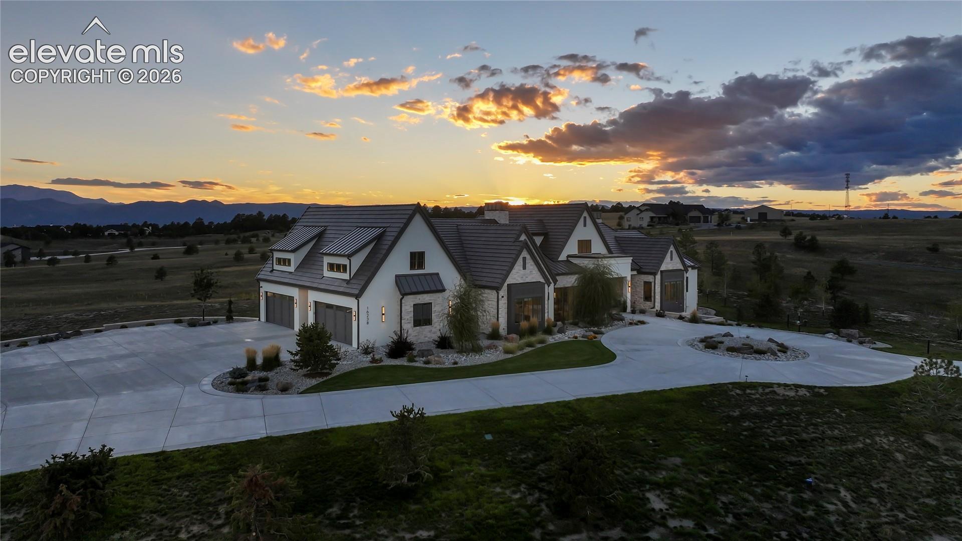 Multi-gabled exterior featuring stone and stucco siding, a tiled roof, multi-car garage, and a spacious concrete driveway with a circular turnaround