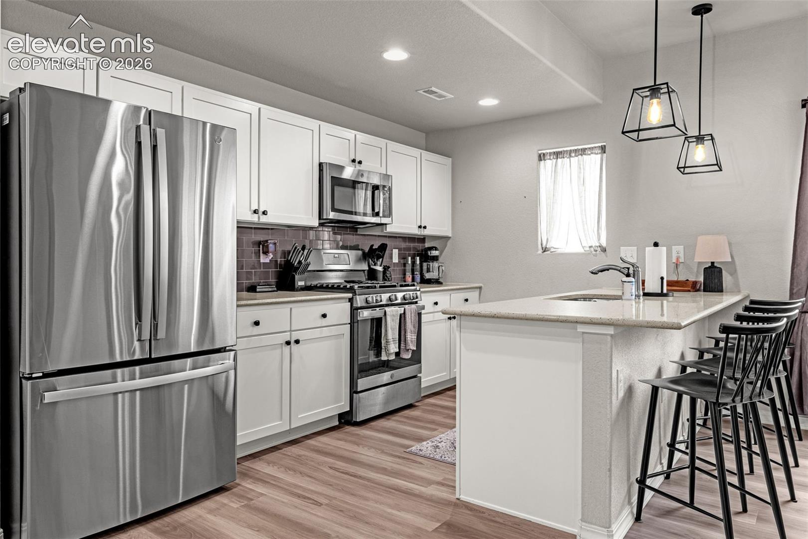 Kitchen featuring stainless steel appliances, white cabinetry, wood-finish flooring, a kitchen island with seating, and pendant lighting