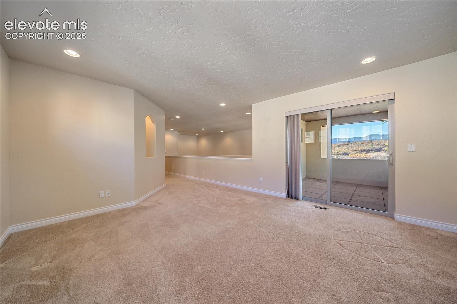 Carpeted flooring, recessed lighting, wall niche, and glass sliding door opening to a tiled covered patio with mountain scenery