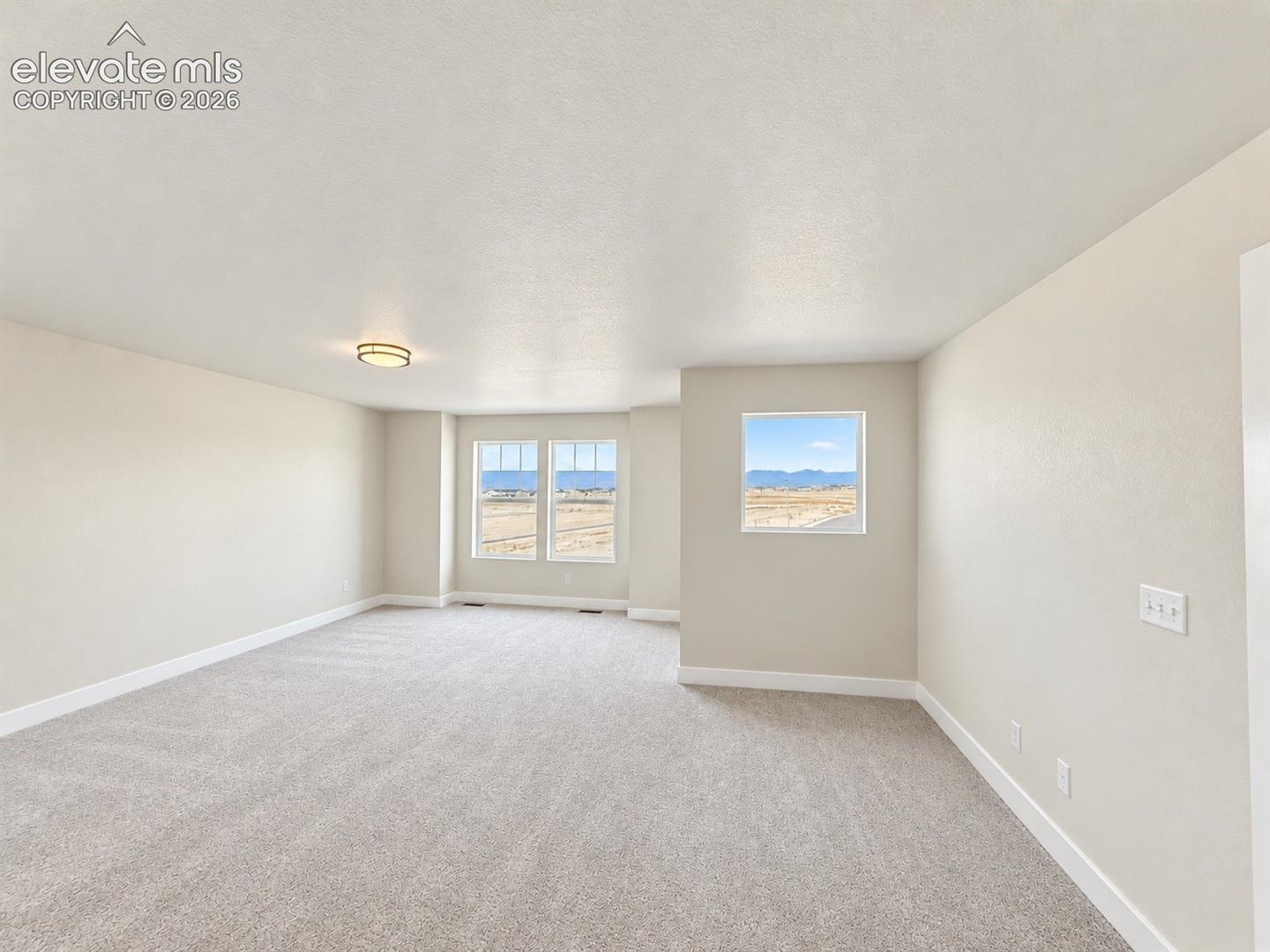 Open-concept interior featuring neutral wall tones, wall-to-wall carpeting, flush-mount lighting, and large windows with mountain scenery