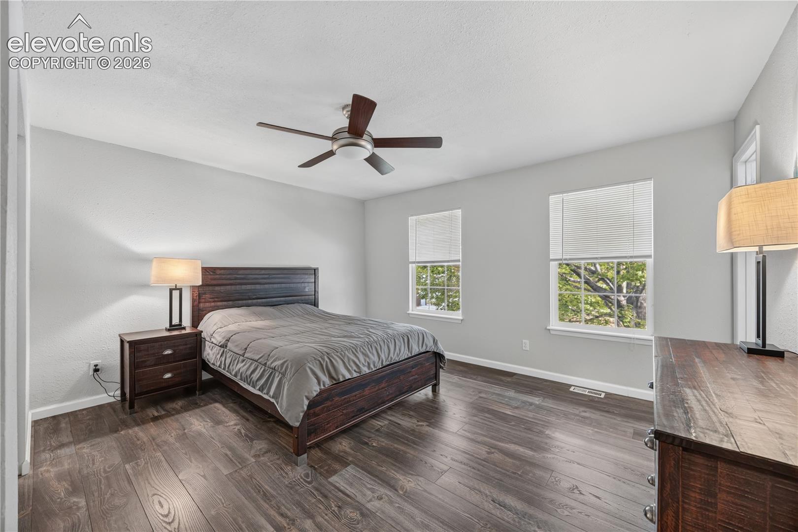 Spacious interior featuring wood-finish flooring, two multi-pane windows with integrated blinds, and a central ceiling fan