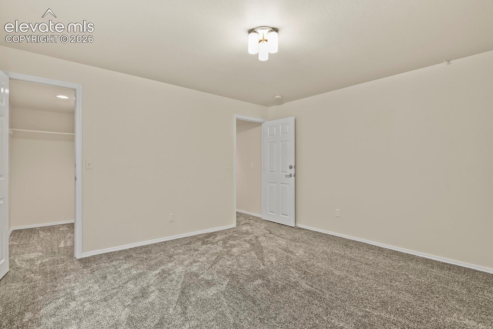 Neutral-toned interior featuring wall-to-wall carpeting, multi-panel doors, and a triple-globe flush-mount light fixture