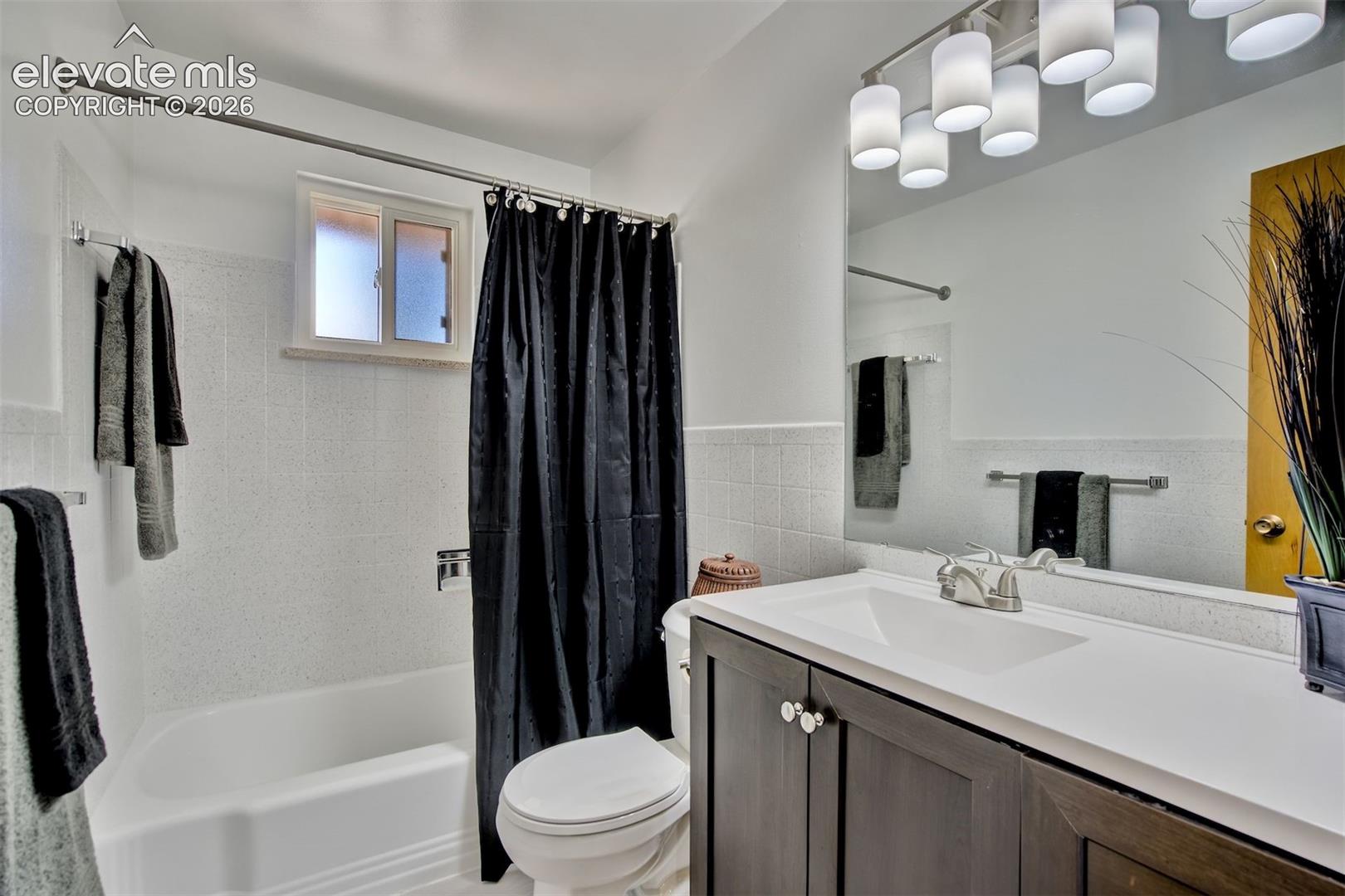 Bathroom featuring a vanity with dark cabinetry, a solid-surface countertop with an integrated basin, a multi-light fixture, and a tub-shower combination with tile surround