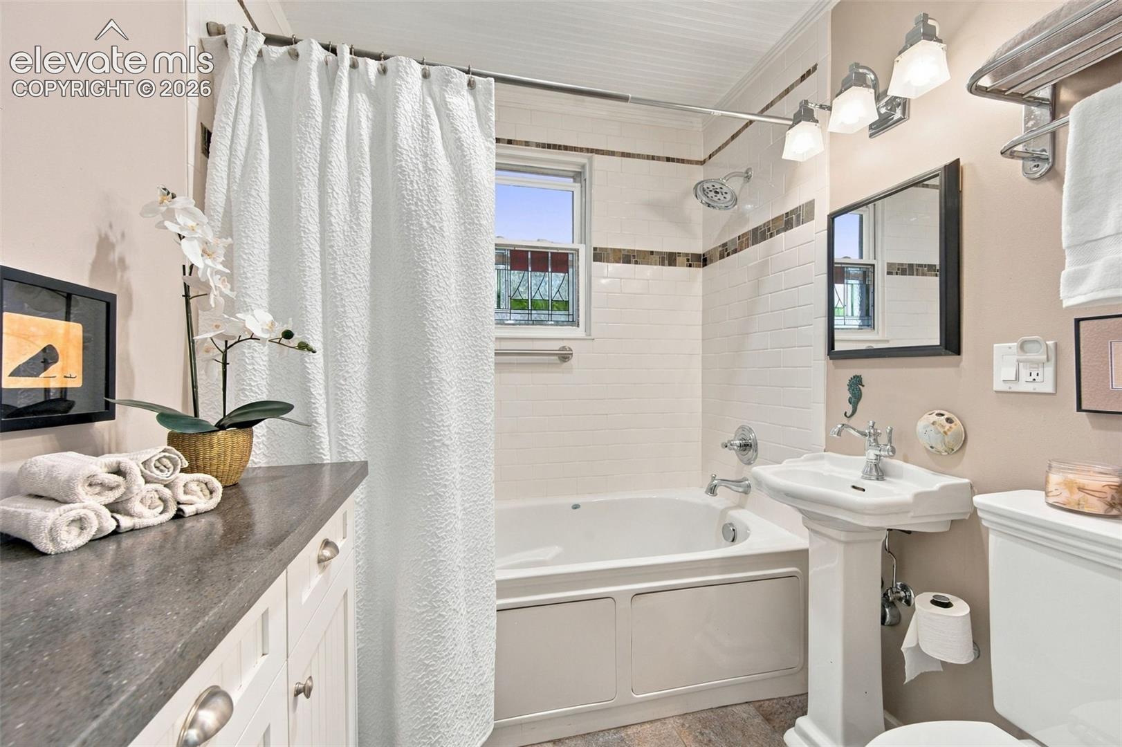 Bathroom featuring a pedestal sink, white subway tile shower surround with decorative inlay, built-in white vanity cabinet with a dark countertop, and polished chrome fixtures