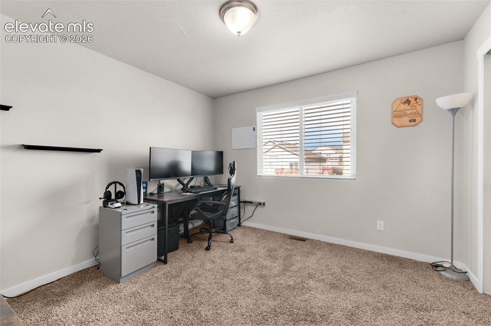 Neutral-toned interior space featuring wall-to-wall carpeting, a flush-mount ceiling light fixture, and a window with horizontal blinds