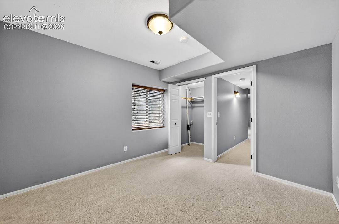 Neutral-toned interior featuring wall-to-wall carpeting, a reach-in closet with built-in shelving, and an operable window with horizontal blinds