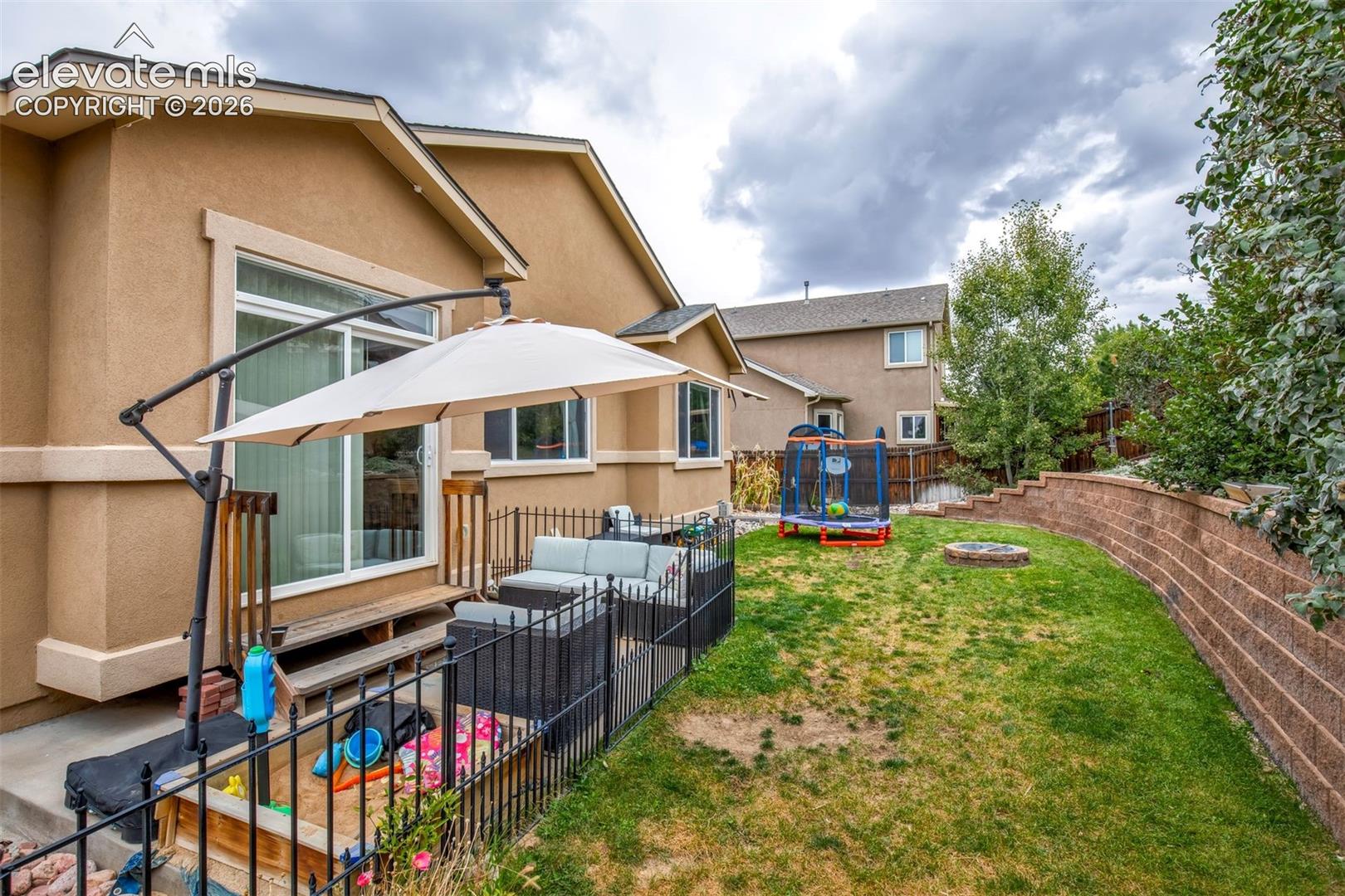 Fully landscaped and fenced backyard with fenced concrete patio, retaining wall, built in firepit and grassy area