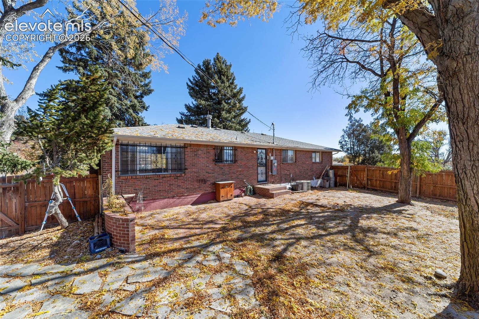 Expansive backyard featuring a red brick exterior, mature trees, a wood privacy fence, and a flagstone patio area