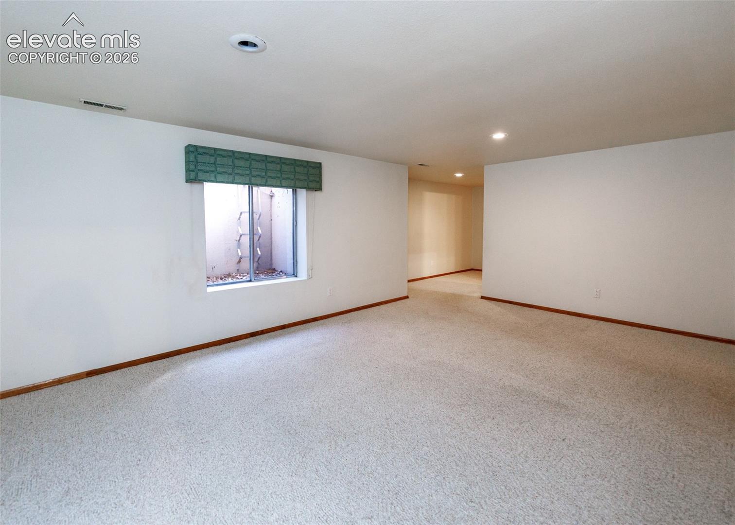 Expansive carpeted room with white walls, a window with a green valance, and recessed ceiling lights