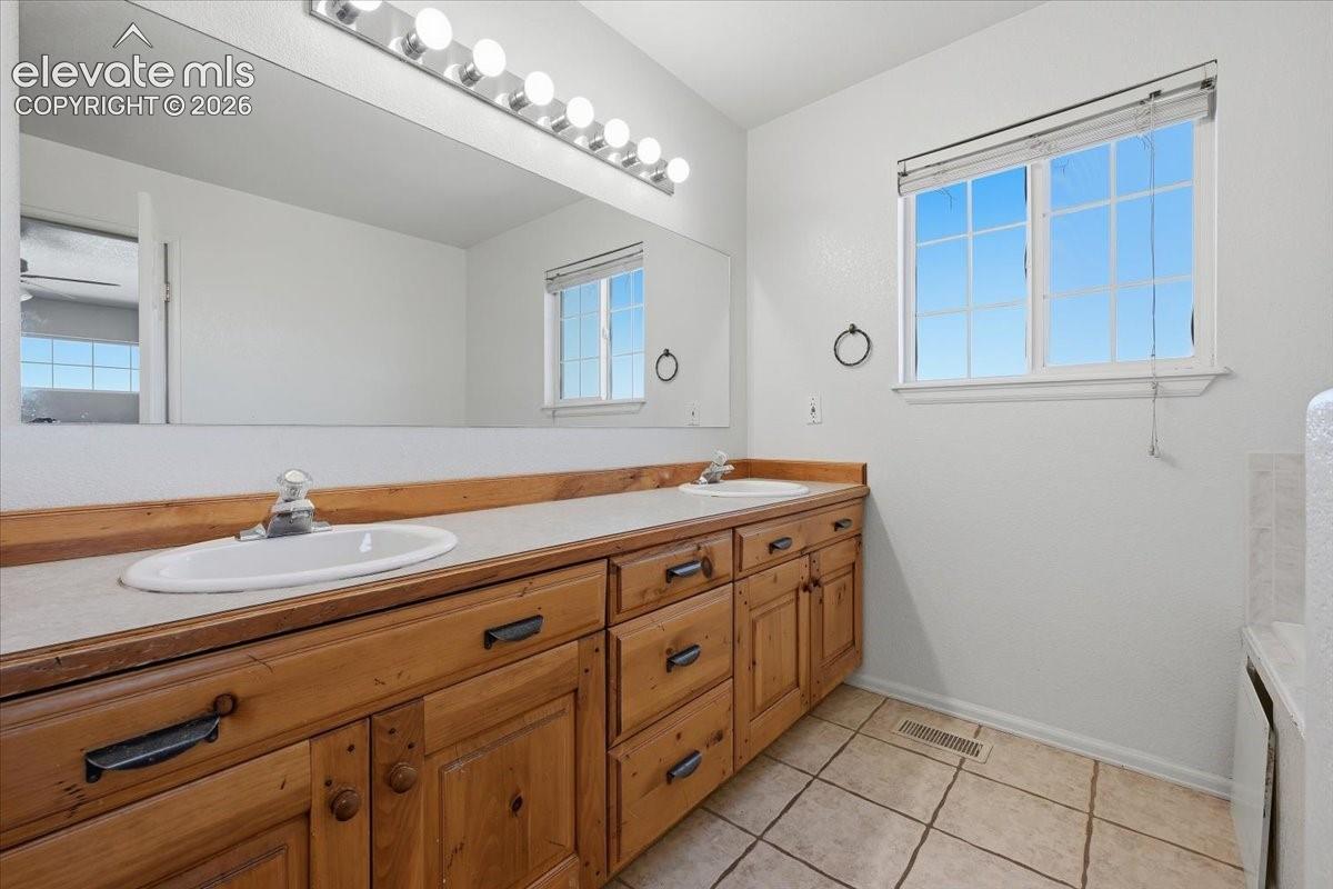 Dual basin vanity with wood-finish cabinetry, a large mirror, and overhead strip lighting