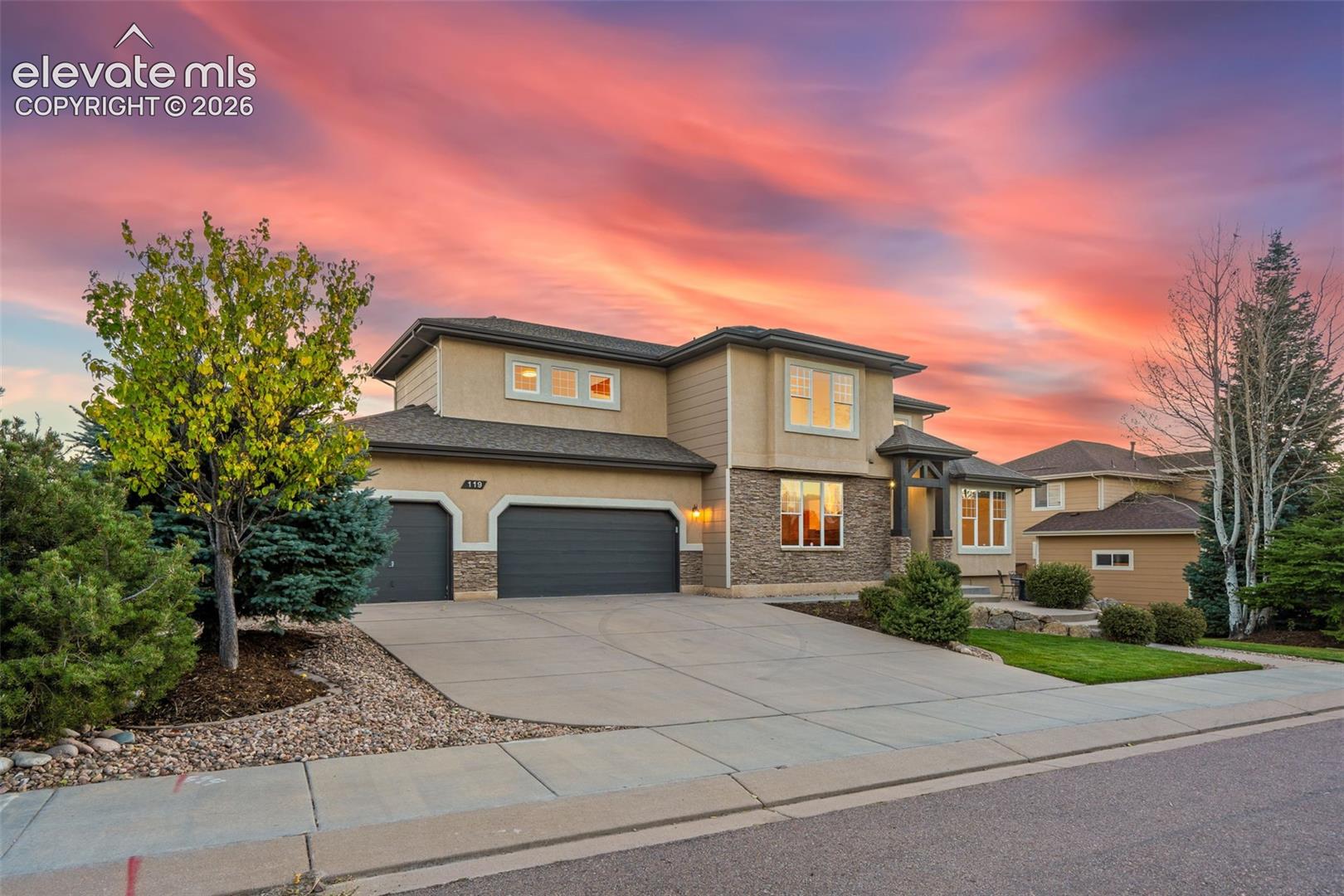 Two-story exterior featuring multi-textured siding, stacked stone accents, a three-car garage, and a concrete driveway