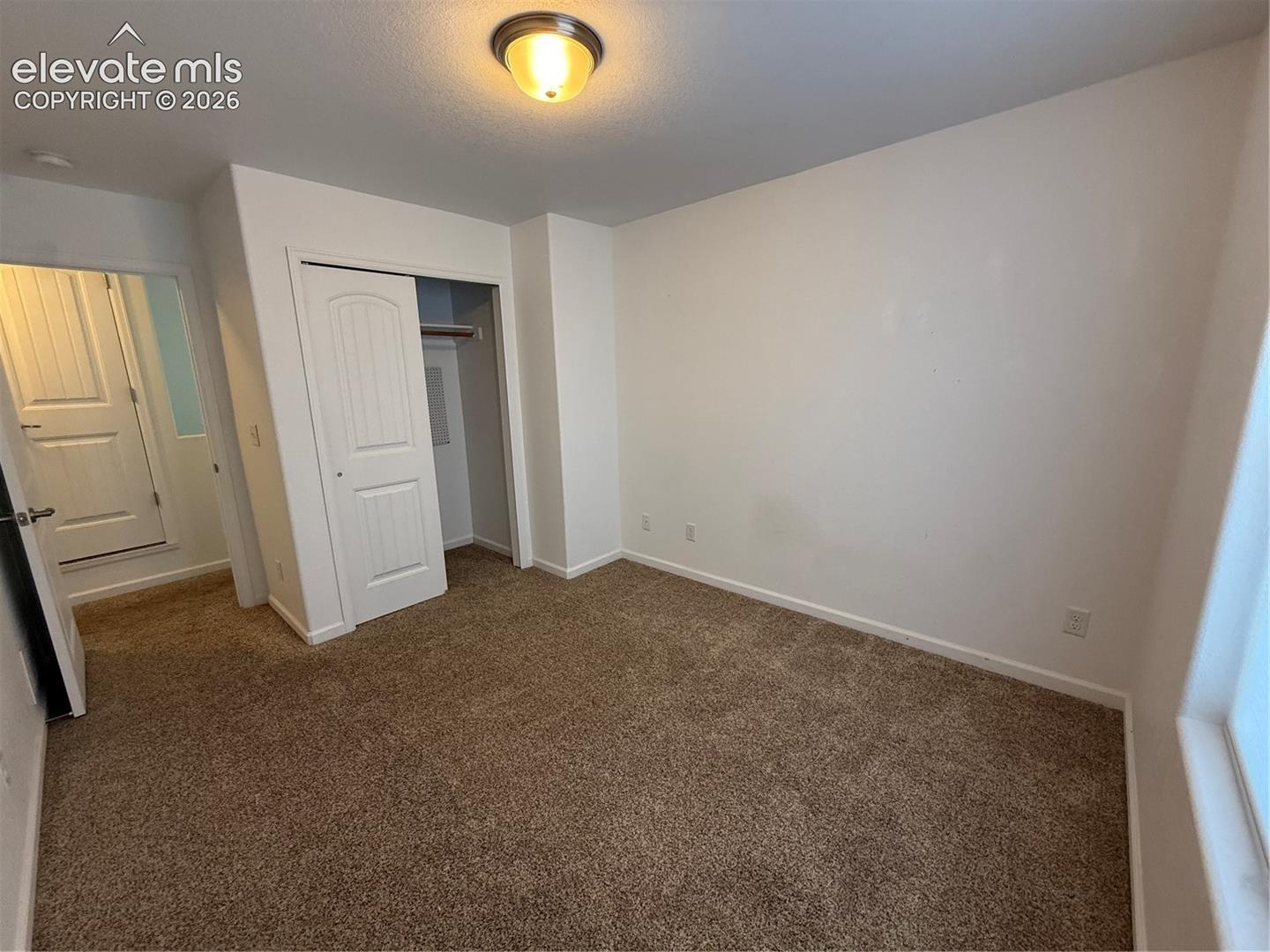 Room featuring neutral-toned carpeting, a built-in closet with a paneled door, and a flush-mount ceiling light fixture