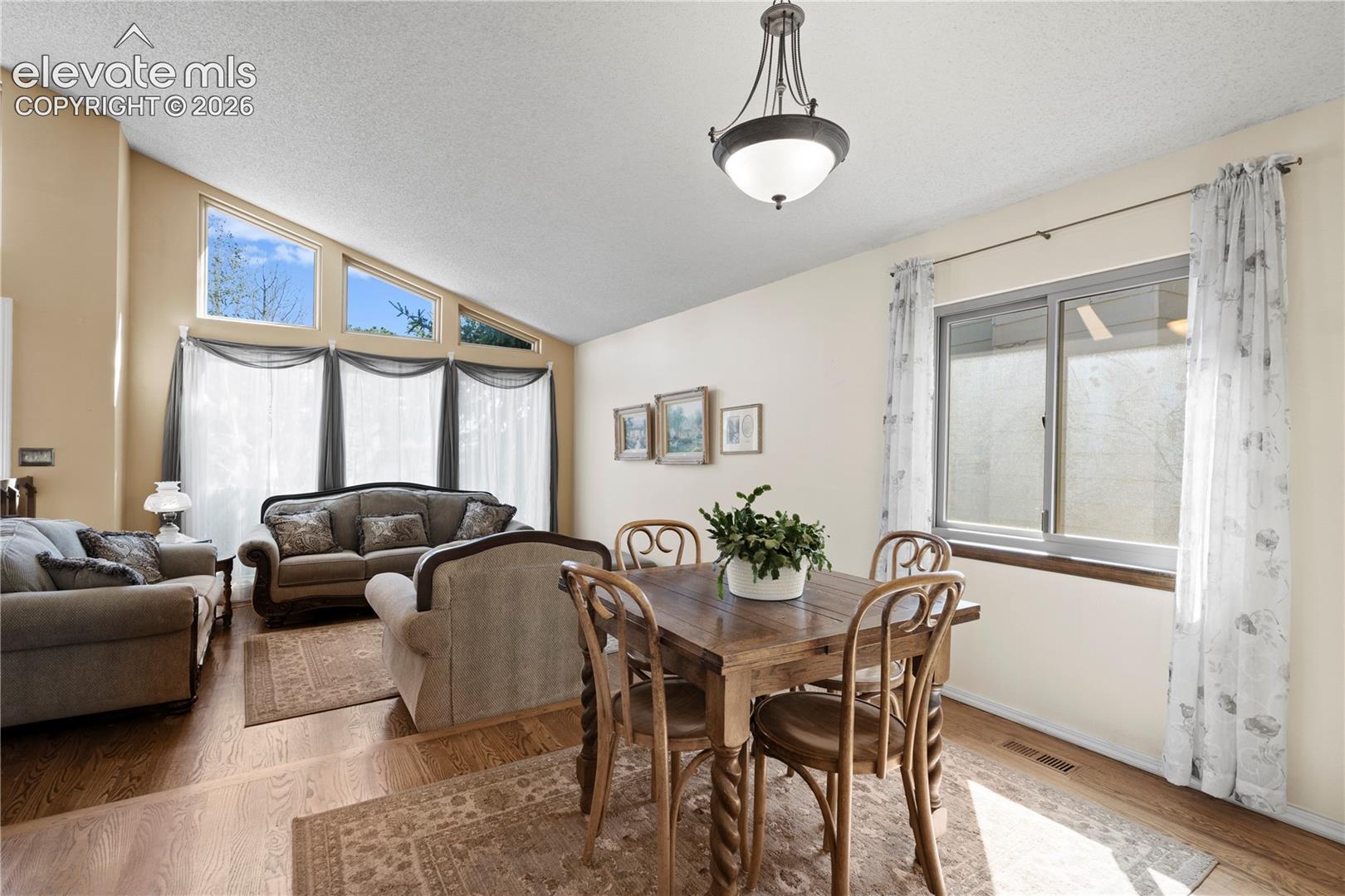 Vaulted ceiling with high windows, wood-finish flooring, and a decorative pendant light fixture