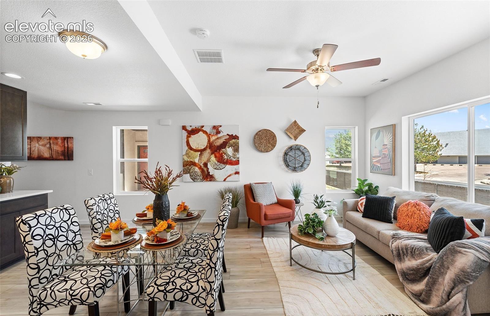 Open-concept common area featuring wood-finish flooring, a ceiling fan with integrated lighting, a flush-mount ceiling light, and large windows