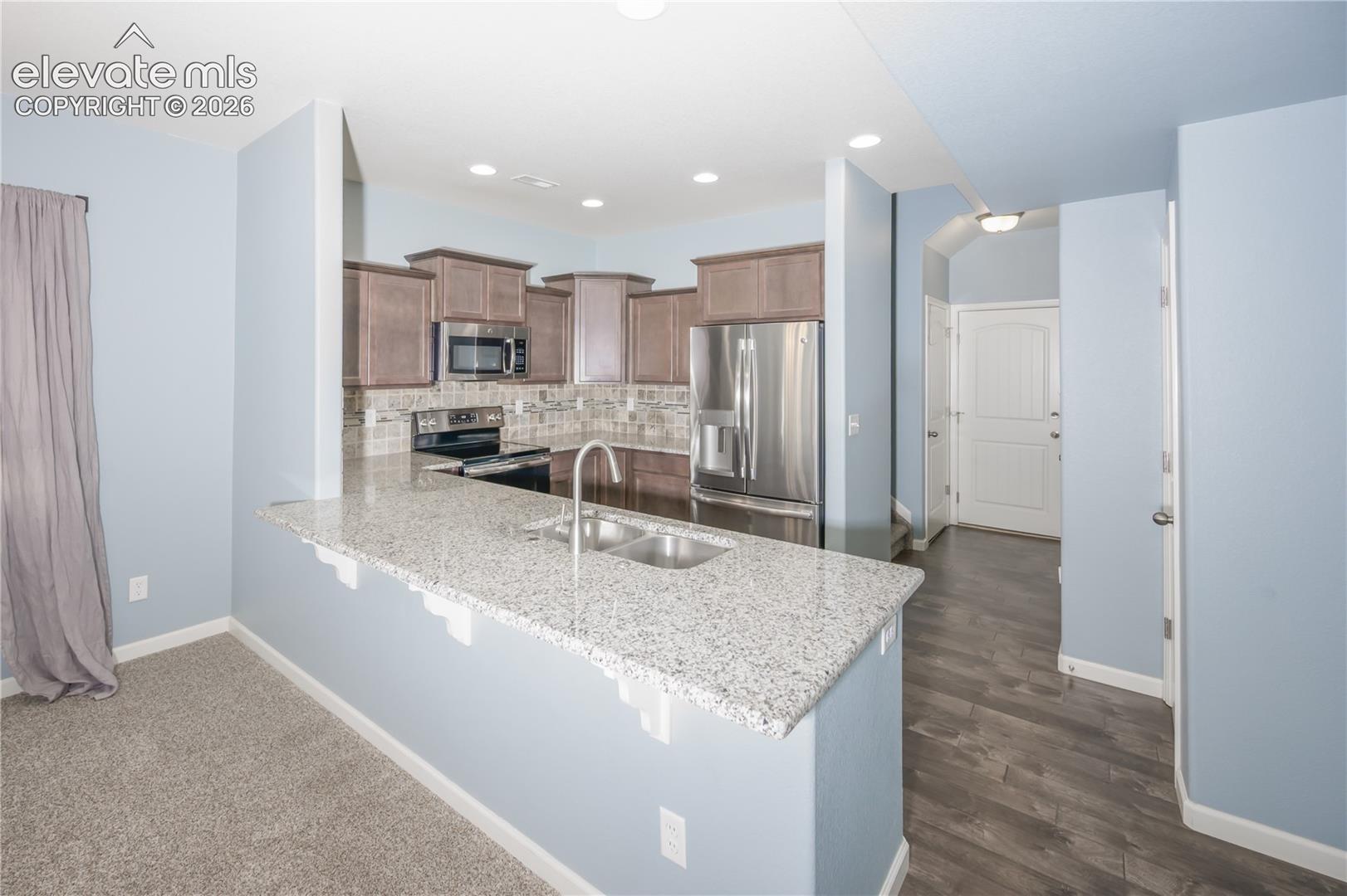 Kitchen featuring stone-finish countertops, stainless steel appliances, dark wood-finish cabinetry, recessed lighting, and a dual-basin undermount sink