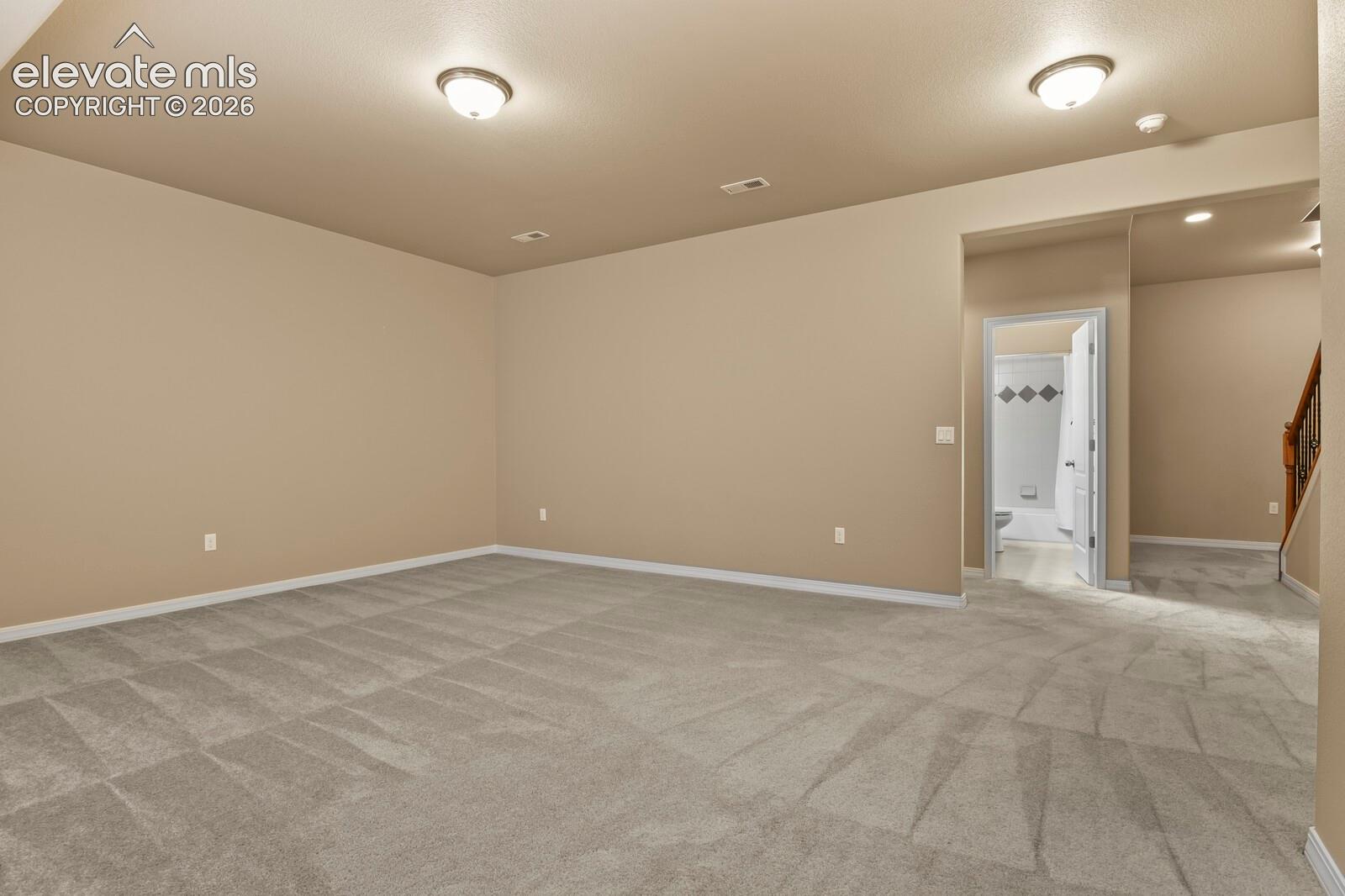 Spacious room with neutral wall tones and patterned carpeting, featuring recessed lighting and a ceiling-mounted light fixture