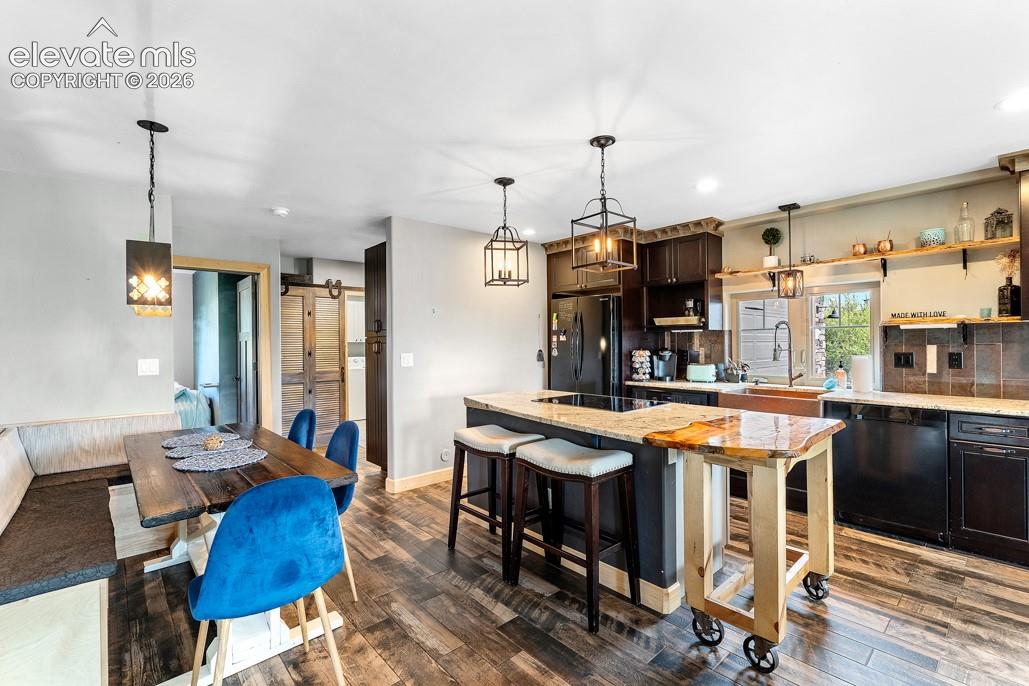 Open-concept kitchen and dining area featuring wood-finish flooring, dark wood cabinetry, a center island with bar seating, and granite countertops