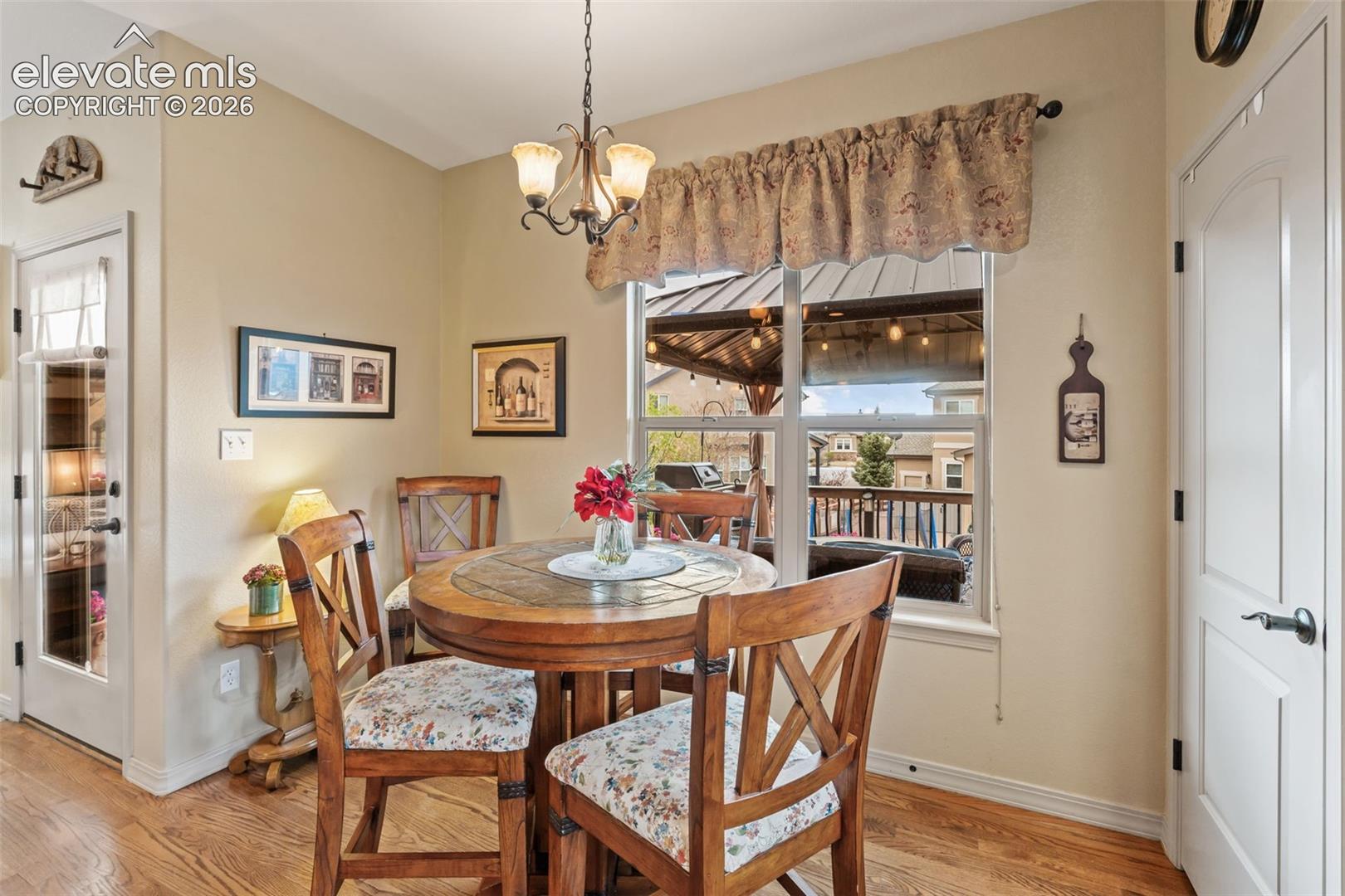 Dining area with wood-finish flooring, a window overlooking an outdoor patio, and a chandelier with glass shades