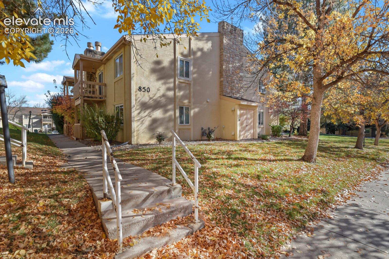 Multi-story exterior featuring stucco siding, stone masonry chimney, private wooden balconies, and concrete walkway with metal handrails