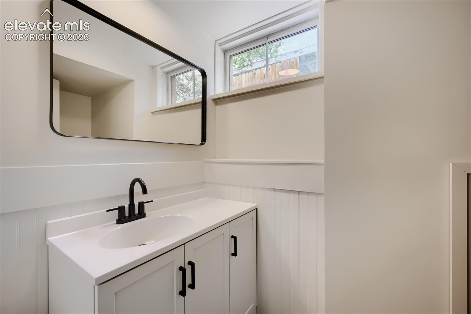 White vanity with a solid surface countertop, undermount sink, and matte black faucet
