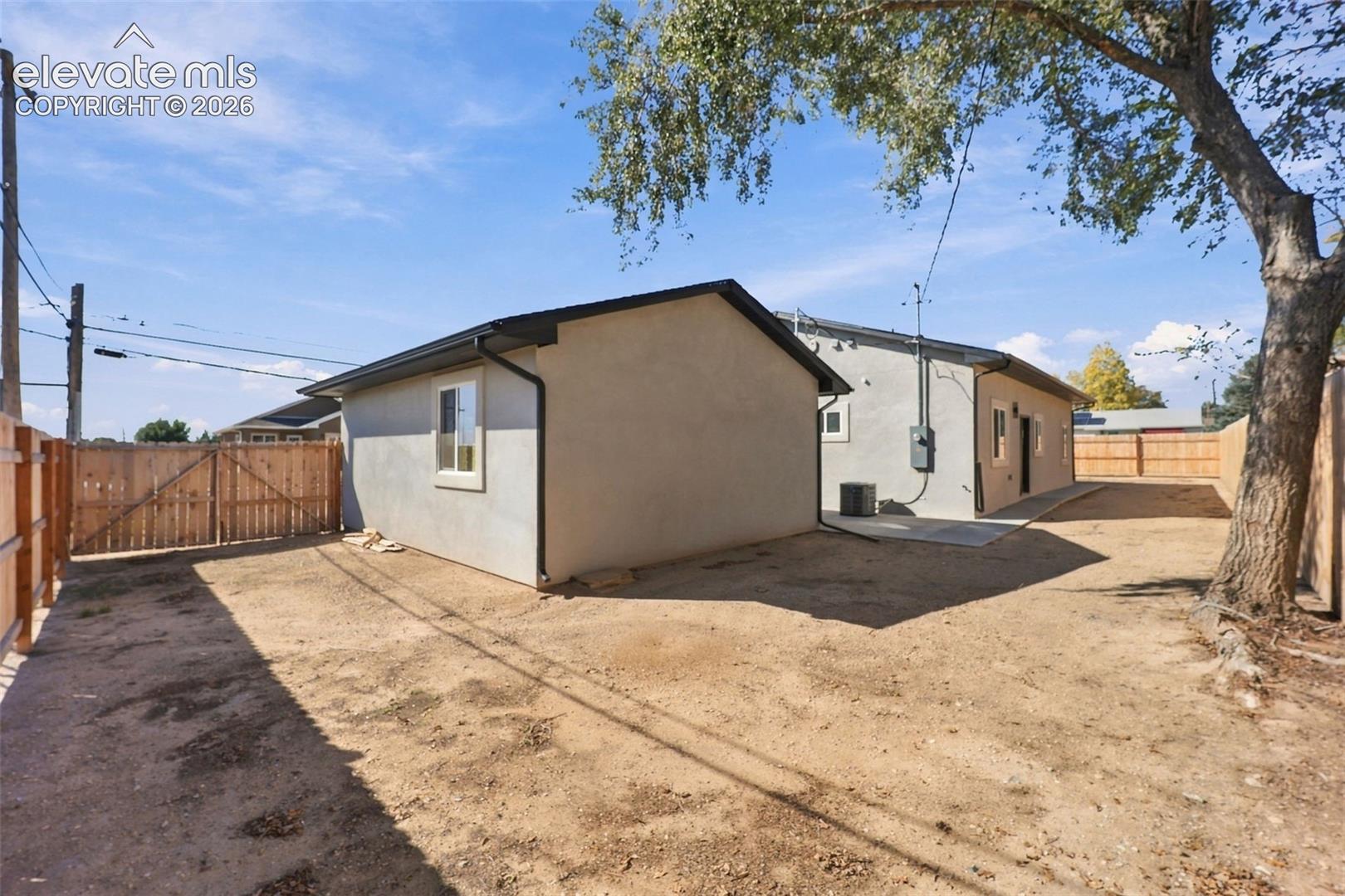 Expansive rear yard with a wood fence, concrete patio, and mature tree