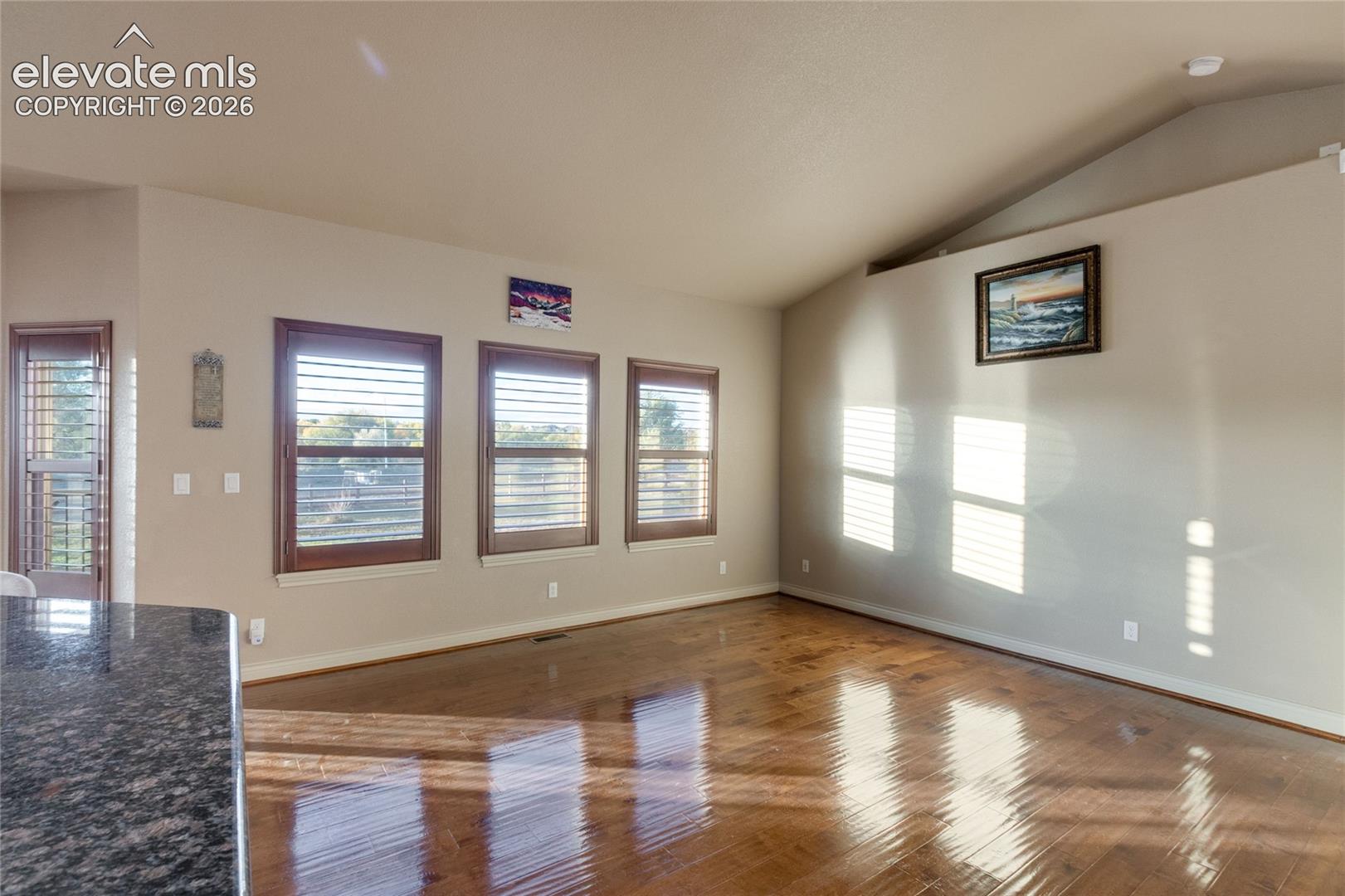 Vaulted ceilings, wood flooring, and natural light through windows featuring plantation shutters
