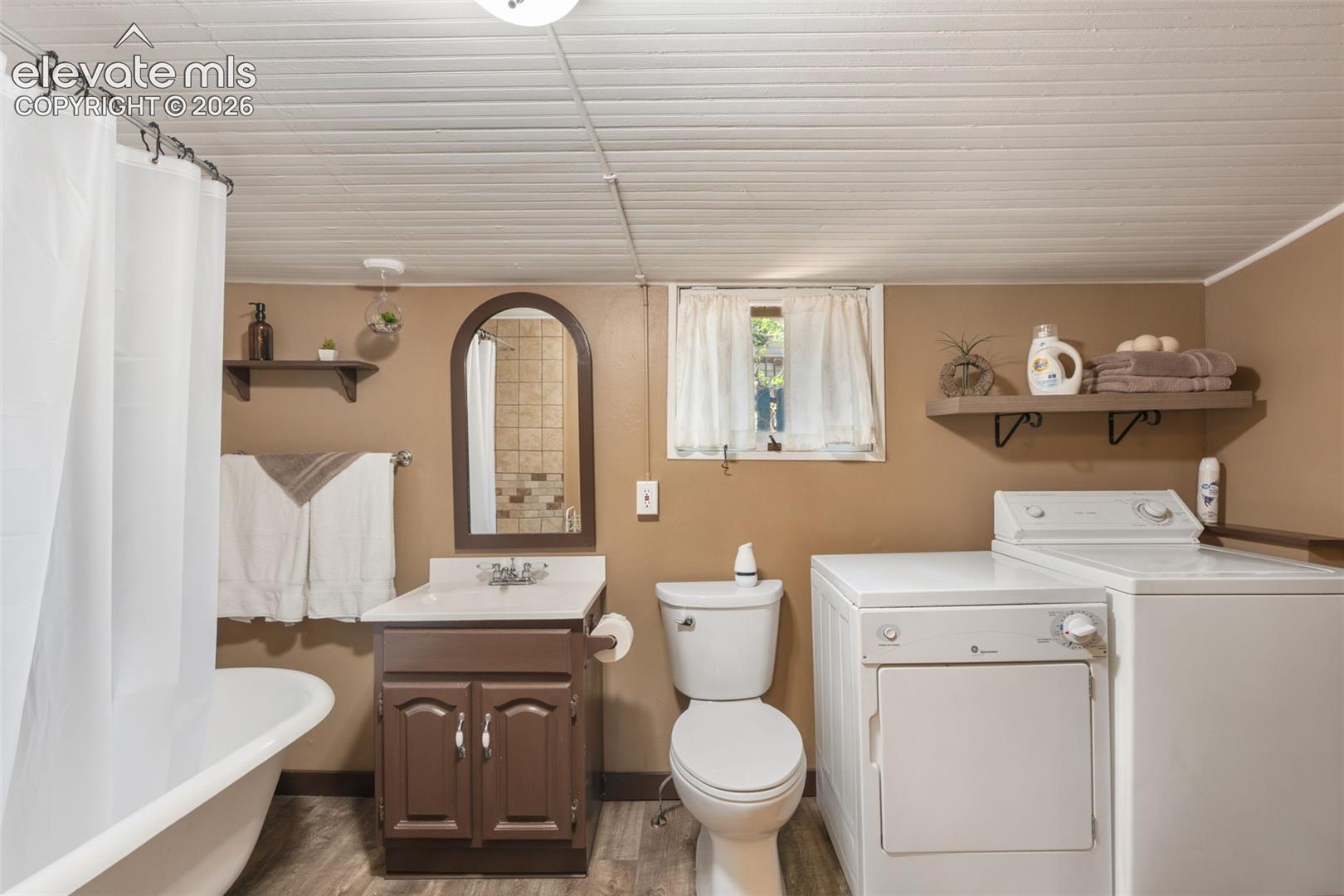 Full bathroom featuring a freestanding tub with shower, wood-finish flooring, a vanity with under-sink storage, and an arched mirror