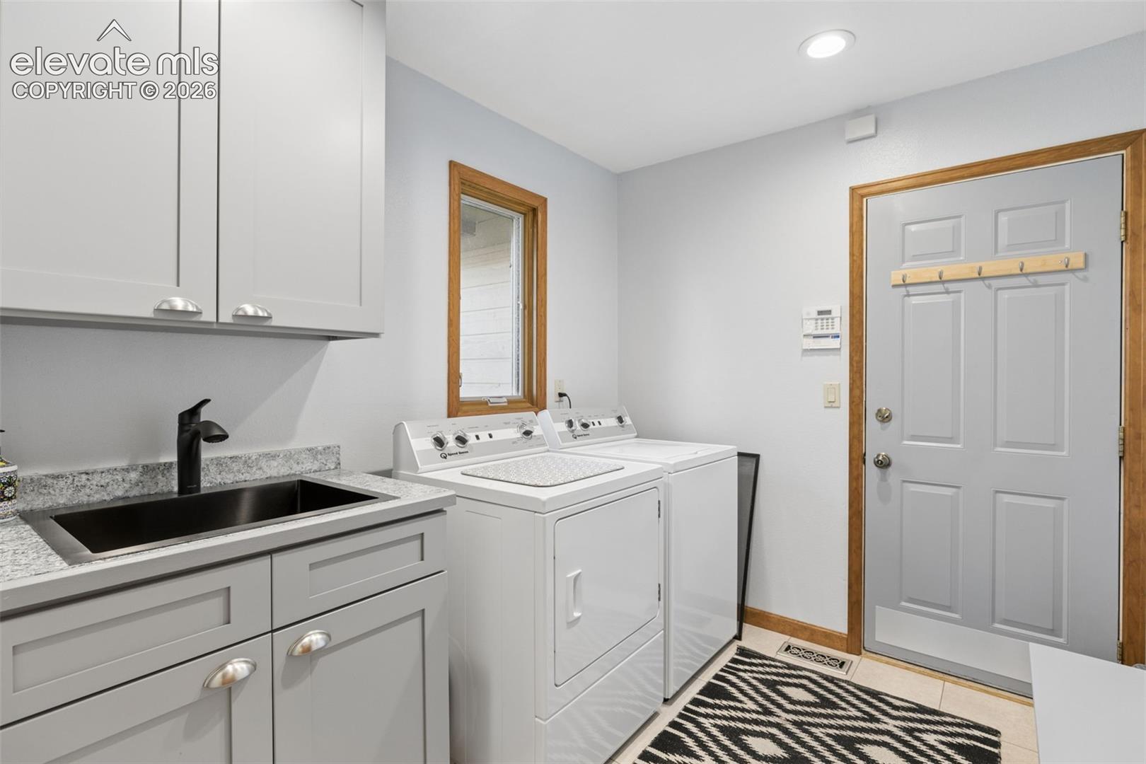 Laundry room featuring shaker-style cabinetry, a drop-in sink with matte black faucet, stone-finish countertops, and an exterior door with wood-finish trim