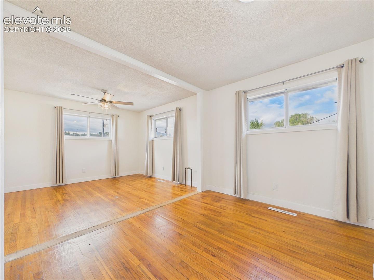 Oversized bedroom created by combining two rooms, featuring hardwood flooring, multiple windows, and a ceiling fan.