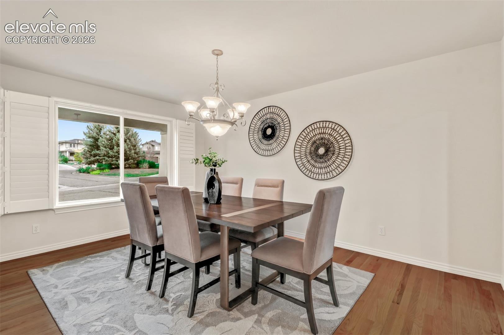 Dining space featuring wood-finish flooring, white plantation shutters, and a multi-arm chandelier