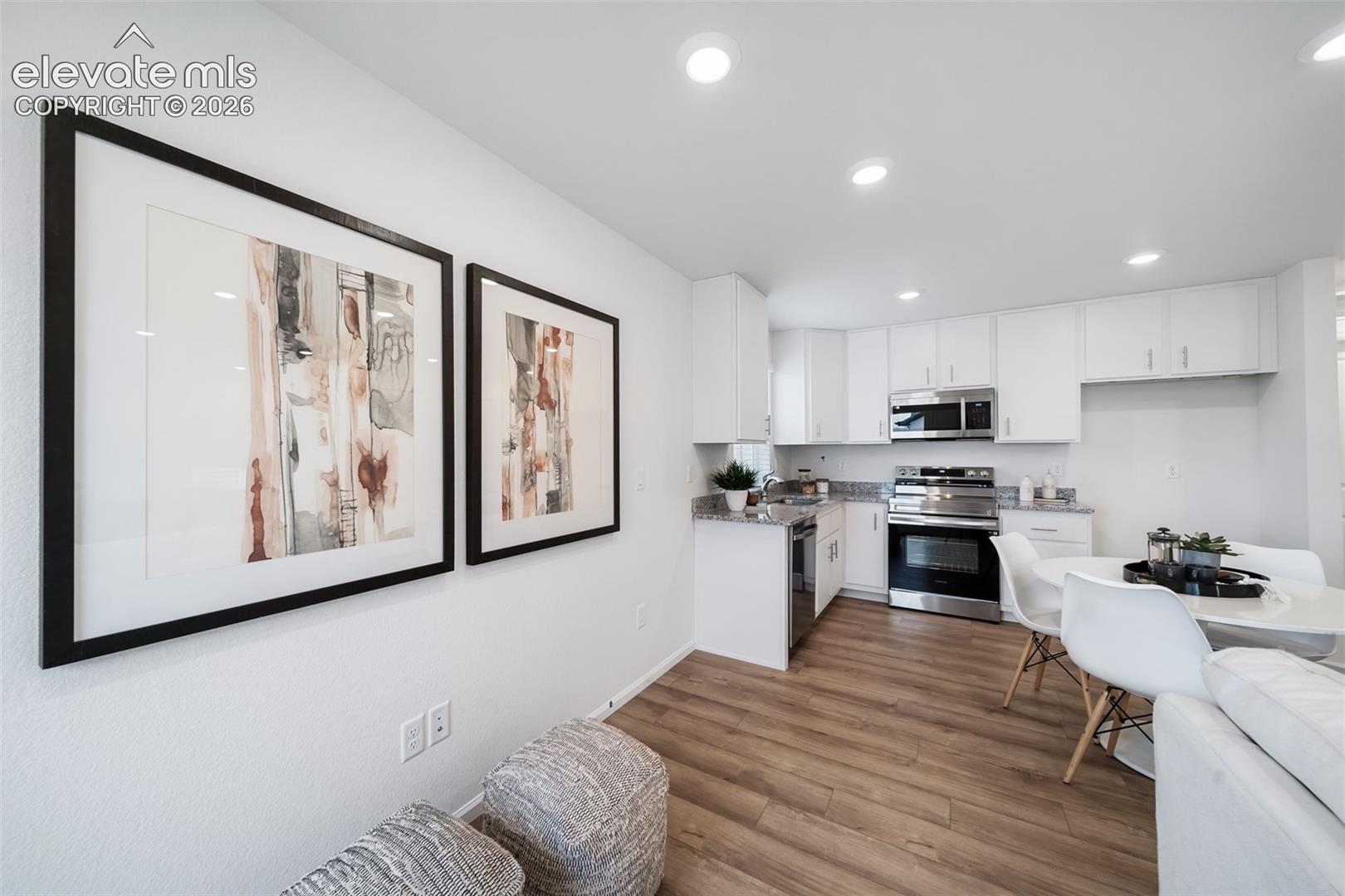Modern kitchen with white cabinetry, stainless steel appliances, recessed lighting, wood-finish flooring, and light-toned countertops